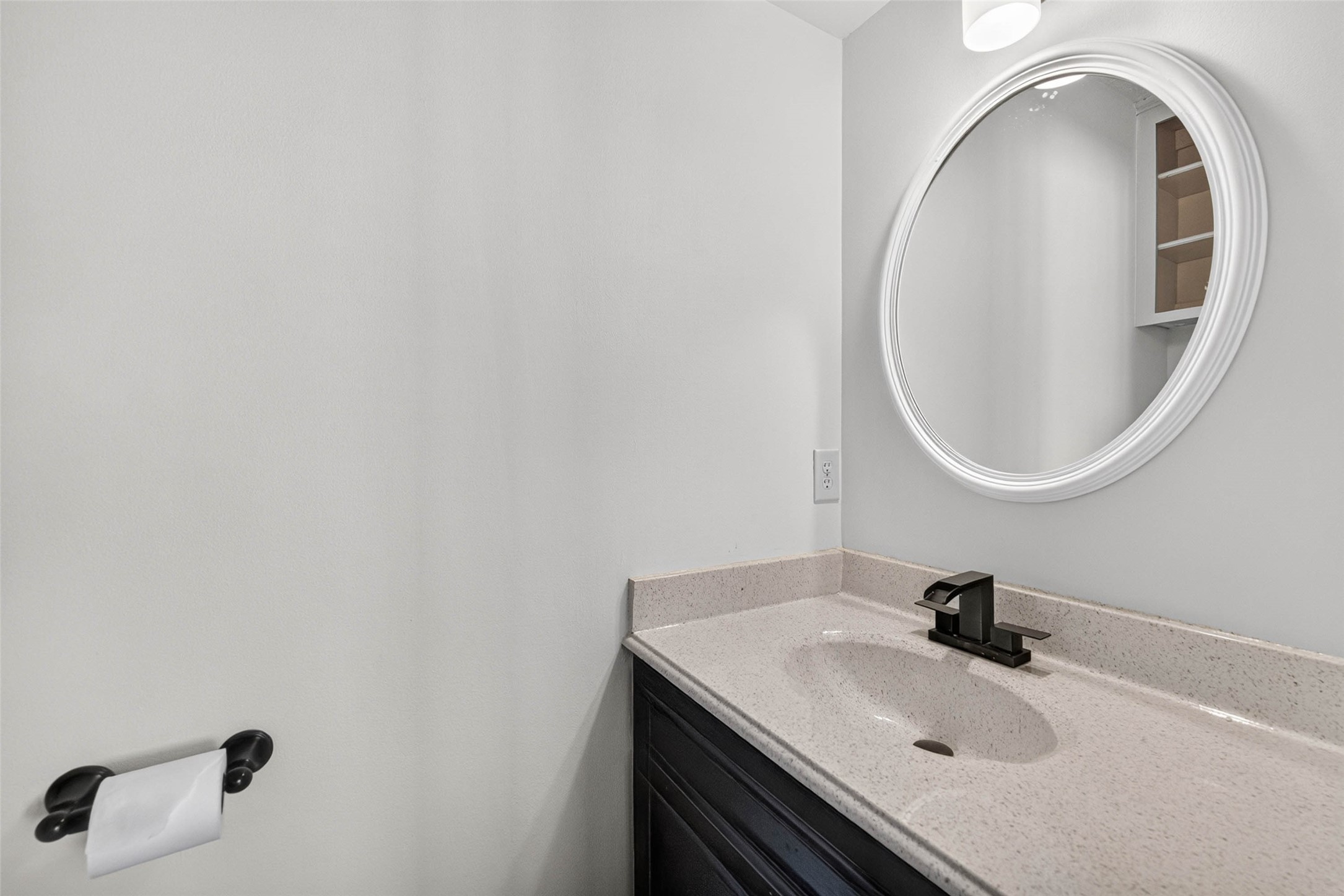 Half bathroom with a single dark-wood vanity, speckled countertop, black faucet, and a large round mirror.