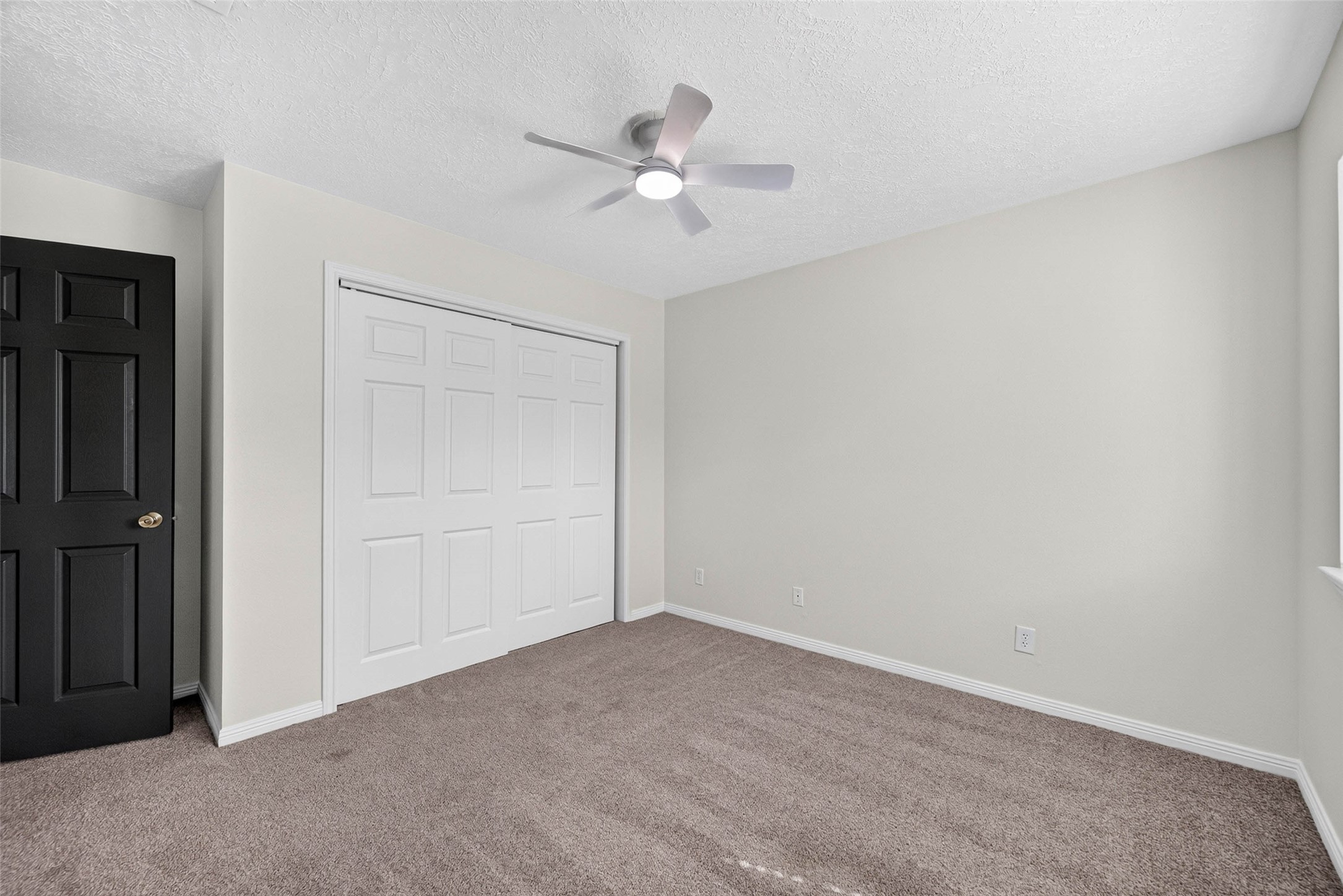 Carpeted bedroom with sliding closet doors, a dark interior door, and a ceiling fan with light.