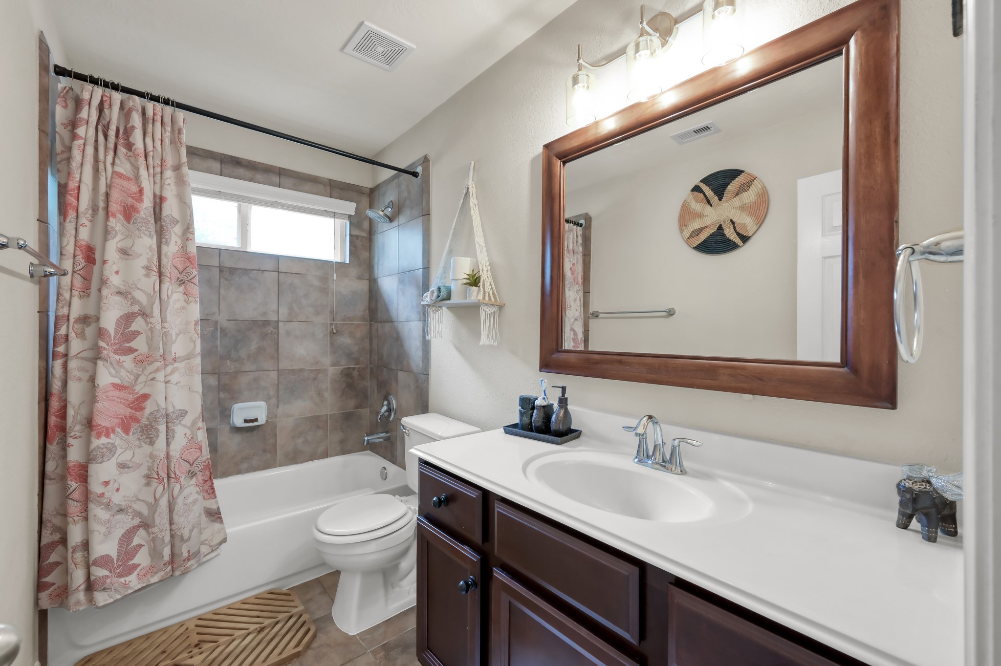 Beautiful full bath featuring tiled shower surround, oversized mirror, updated lighting, and plenty of counter space for everyday convenience.