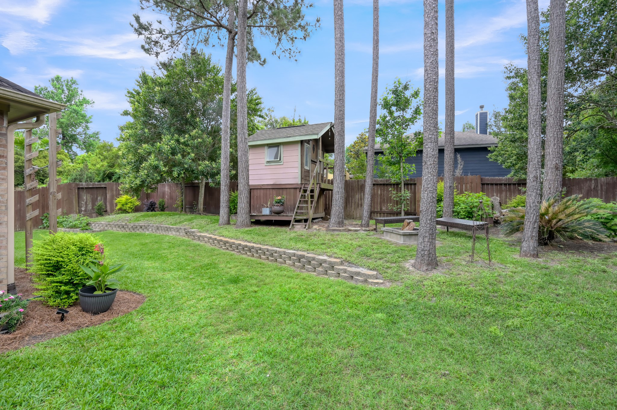 Charming backyard complete with a whimsical elevated playhouse, fire pit area, mature trees, and a park-like setting perfect for enjoying the outdoors.