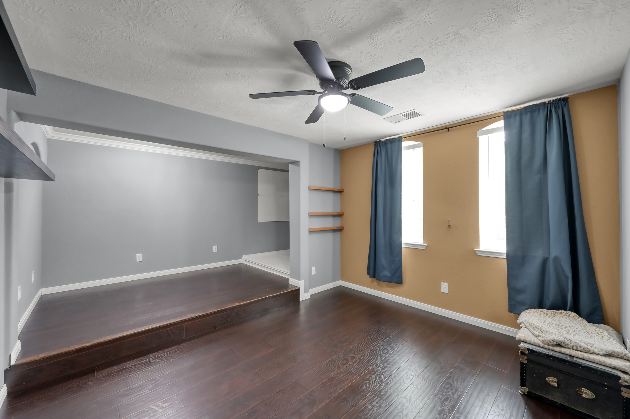 Enormous secret room with rich wood flooring and elevated platform area, offering endless possibilities for a studio, workout space, game room, or creative retreat.