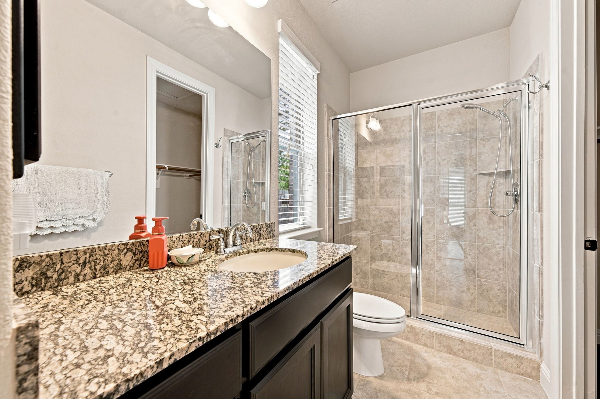 Private bath for the secondary bedroom, featuring a granite vanity, glass-enclosed shower, and adjoining walk-in closet.