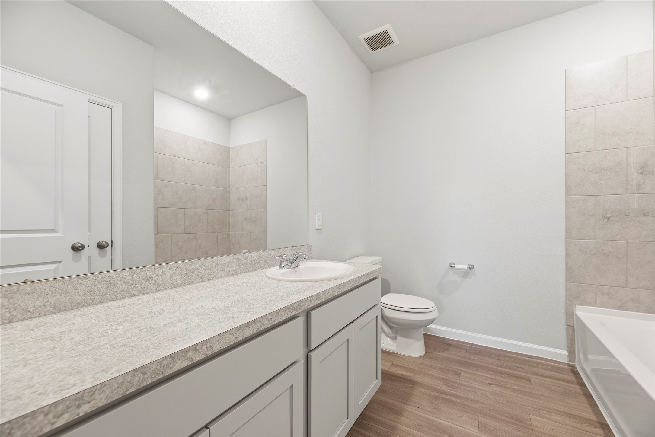 A long vanity offers room to spread out during the morning routine, with cabinet storage below and a tub with a tile surround alongside.
