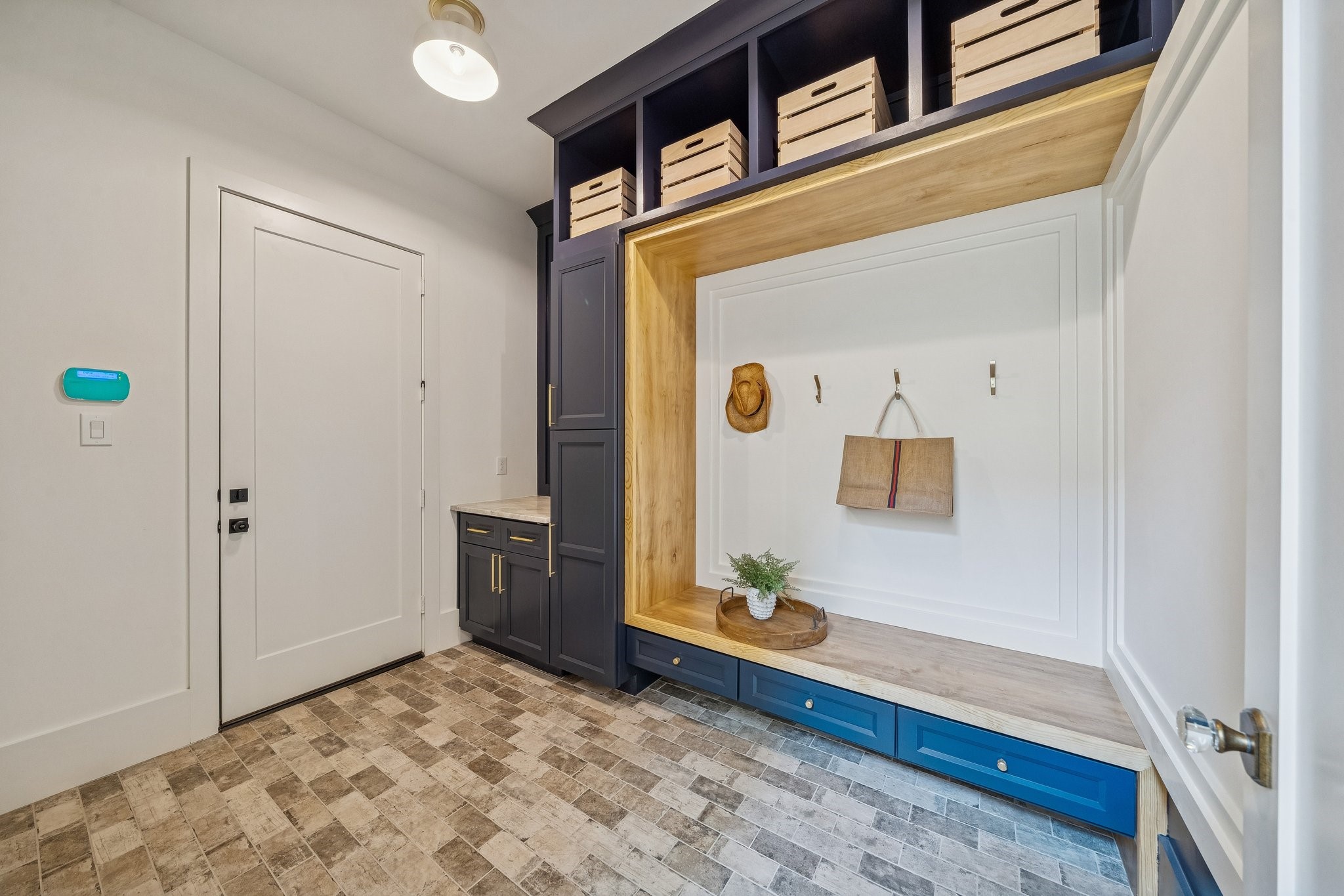 Spacious mud room/utility room with brick flooring and built-in storage cabinets. The door leads to the garage with a keypad for the alarm nearby.