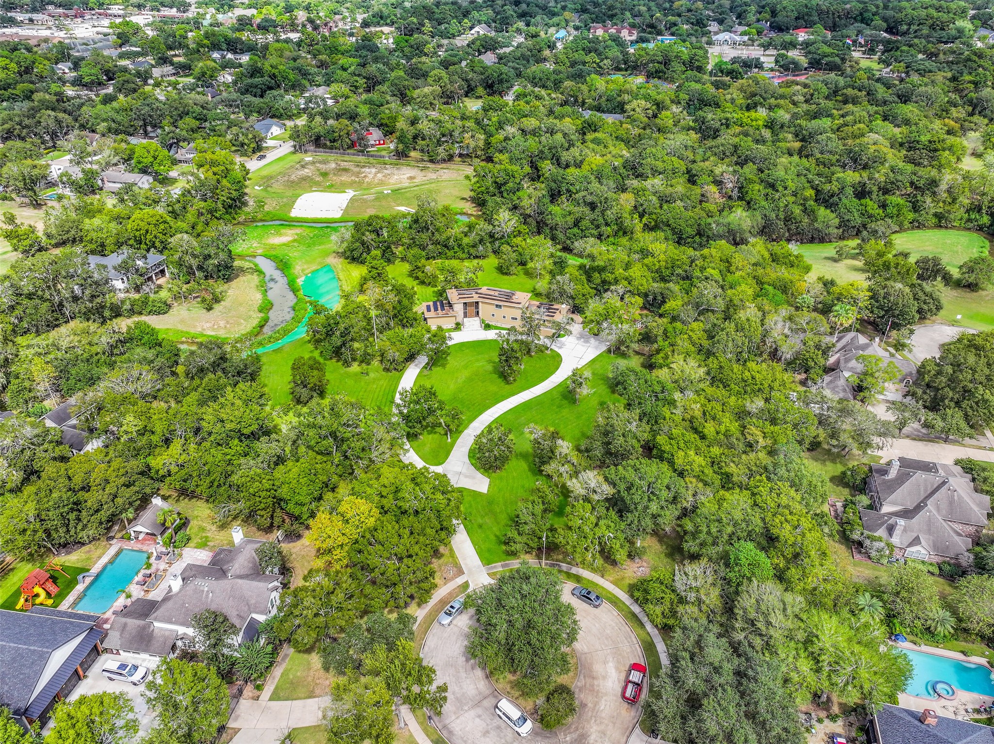 An elevated perspective showcases the home's remarkable setting, with expansive grassy areas, towering shade trees & Cowart Creek winding through portions of the acreage. Enjoy the privacy of this tucked-away property while remaining conveniently close to central Friendswood amenities.