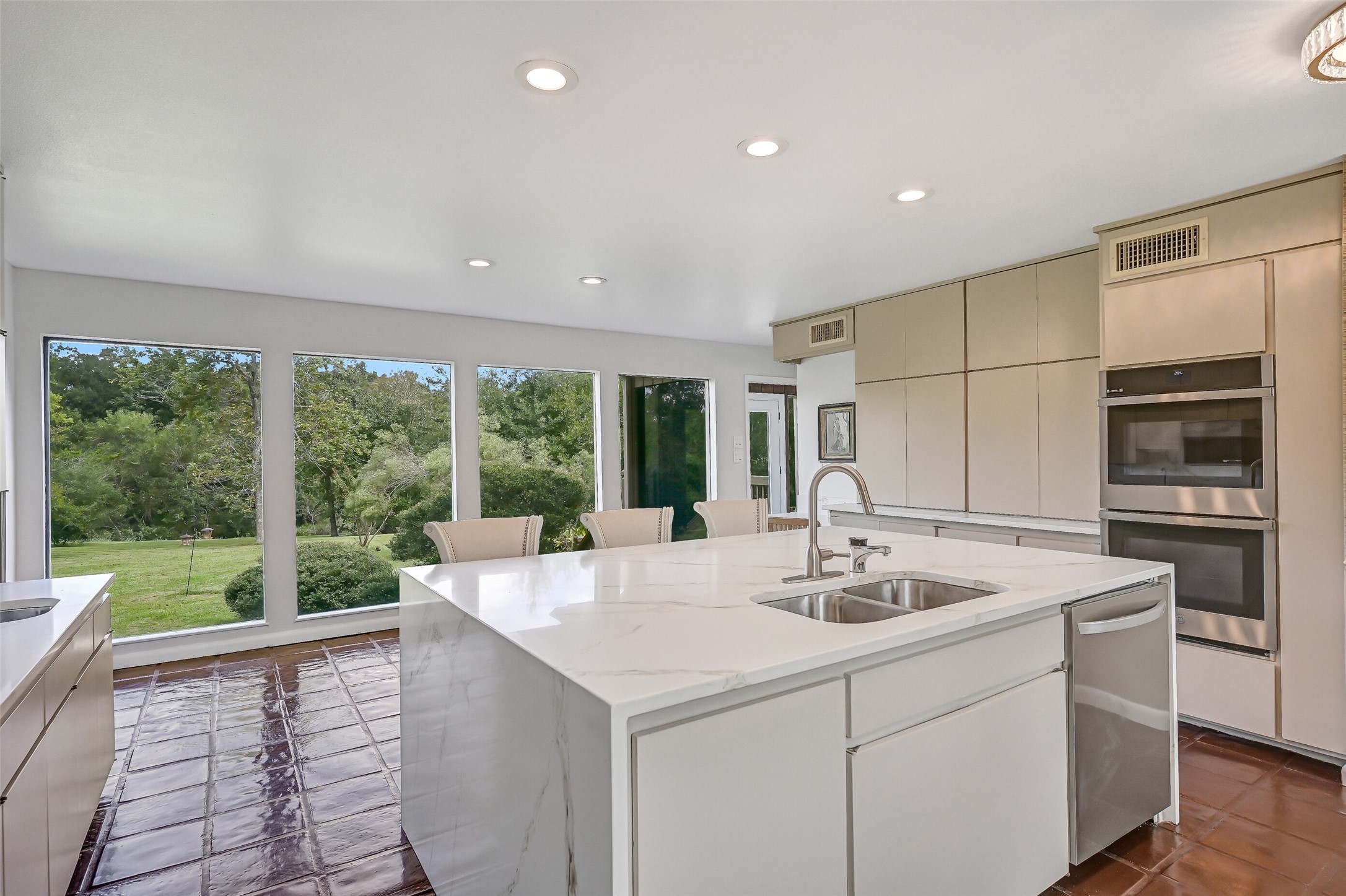 A series of oversized picture windows stretches along the rear of the kitchen, showcasing beautiful views of the expansive lawn & mature trees. The painted tile flooring continues into this light-filled area, which connects the renovated kitchen to the home's adjoining living spaces.