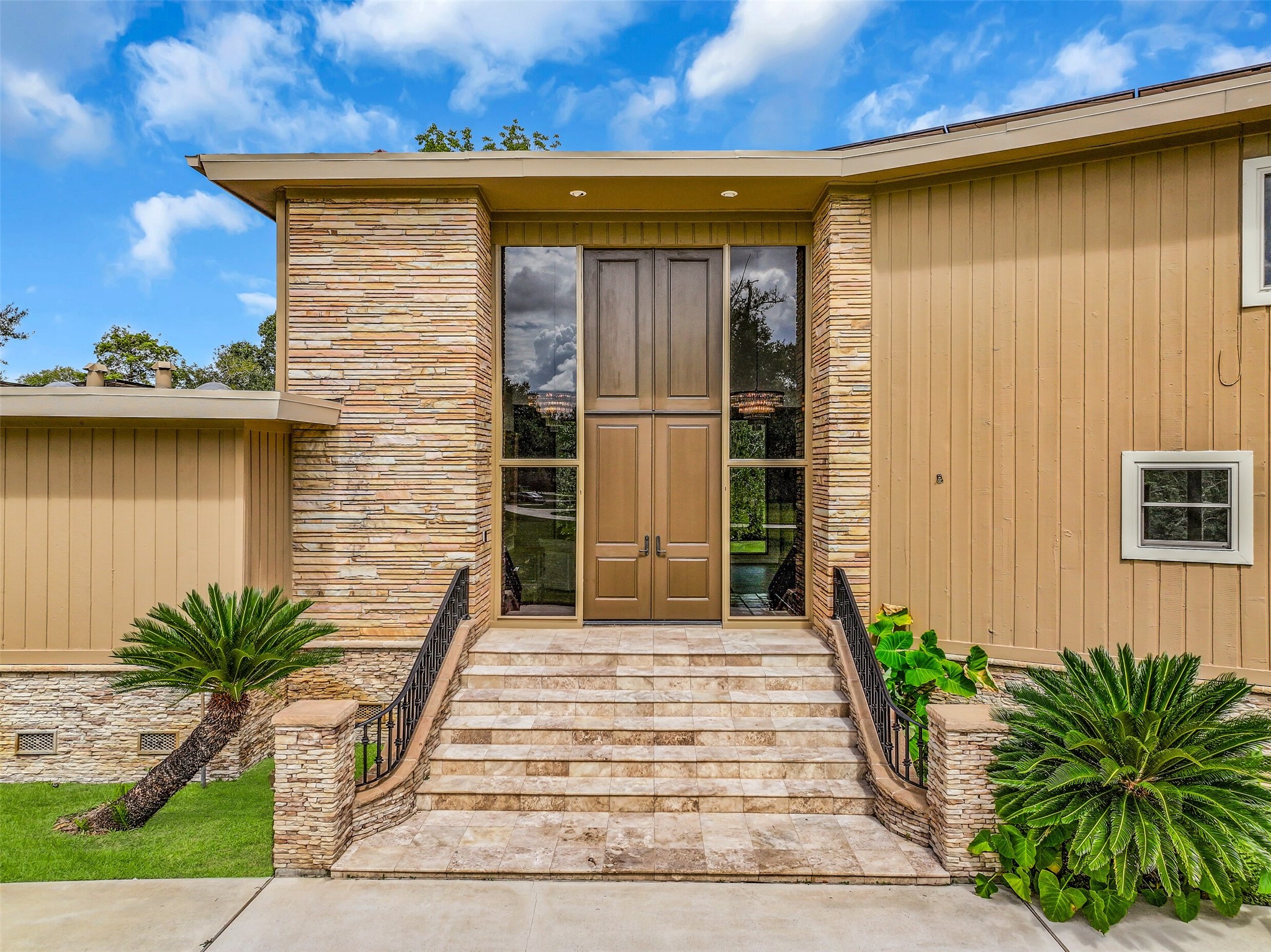 A closer look at the impressive front entrance reveals oversized double doors framed by full-height glass sidelights. The dramatic architectural details continue inside, where a soaring 17' entry ceiling, two grand chandeliers & open-riser staircase create a striking first impression.