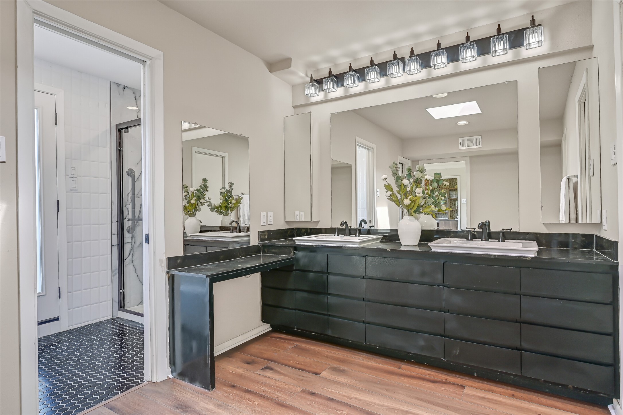 The primary bathroom features an expansive dual-sink vanity with dark cabinetry, generous drawer storage, black countertops & contemporary lighting. A separate dressing vanity adds convenience, while the adjoining bathing area includes an updated shower & recently replaced soaking tub.