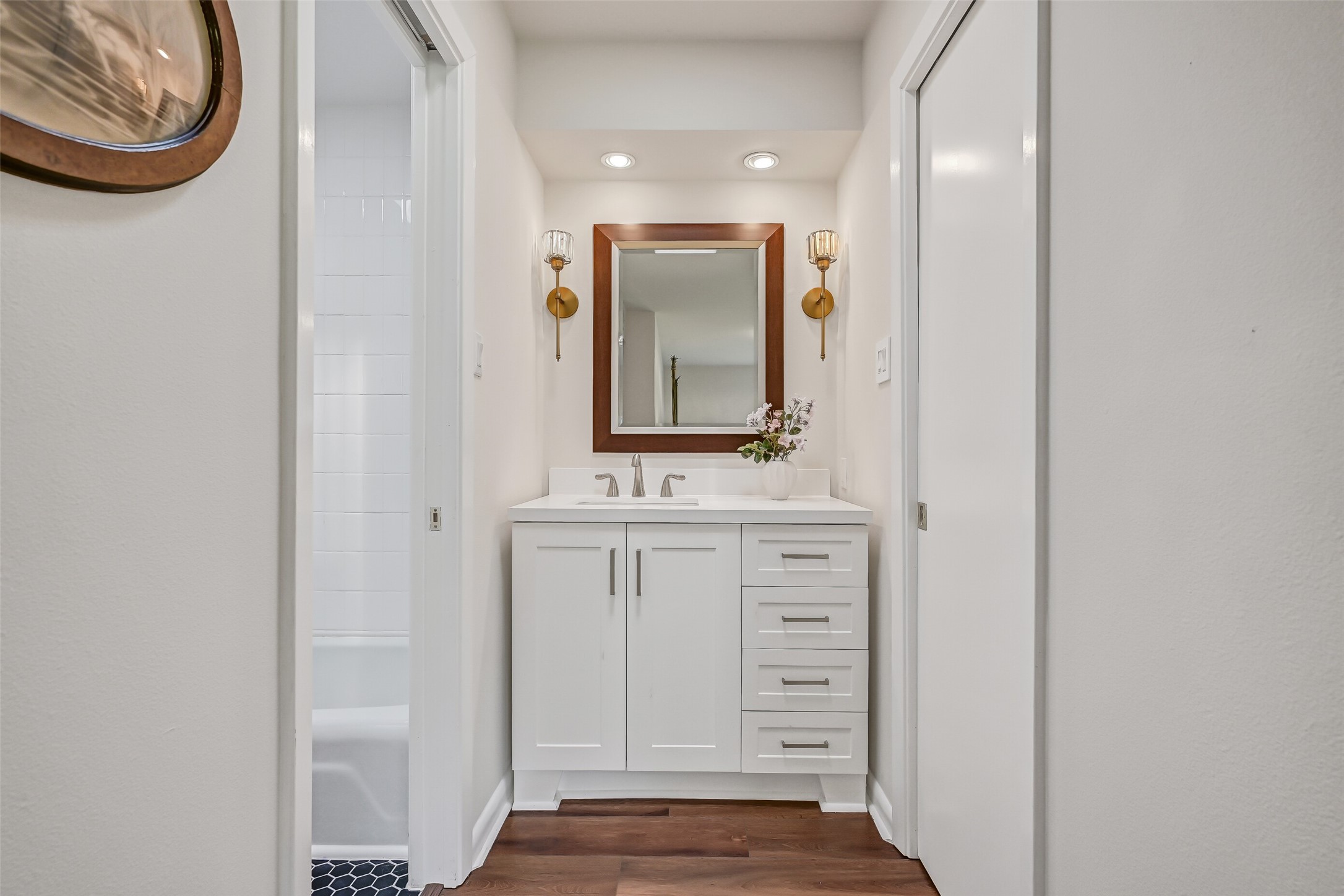 The second private vanity area features updated white cabinetry, a rectangular framed mirror, decorative gold sconces & generous drawer storage. Located just outside the shared bathing area, this thoughtfully arranged Jack & Jill bathroom provides separate grooming spaces for the adjoining bedrooms.