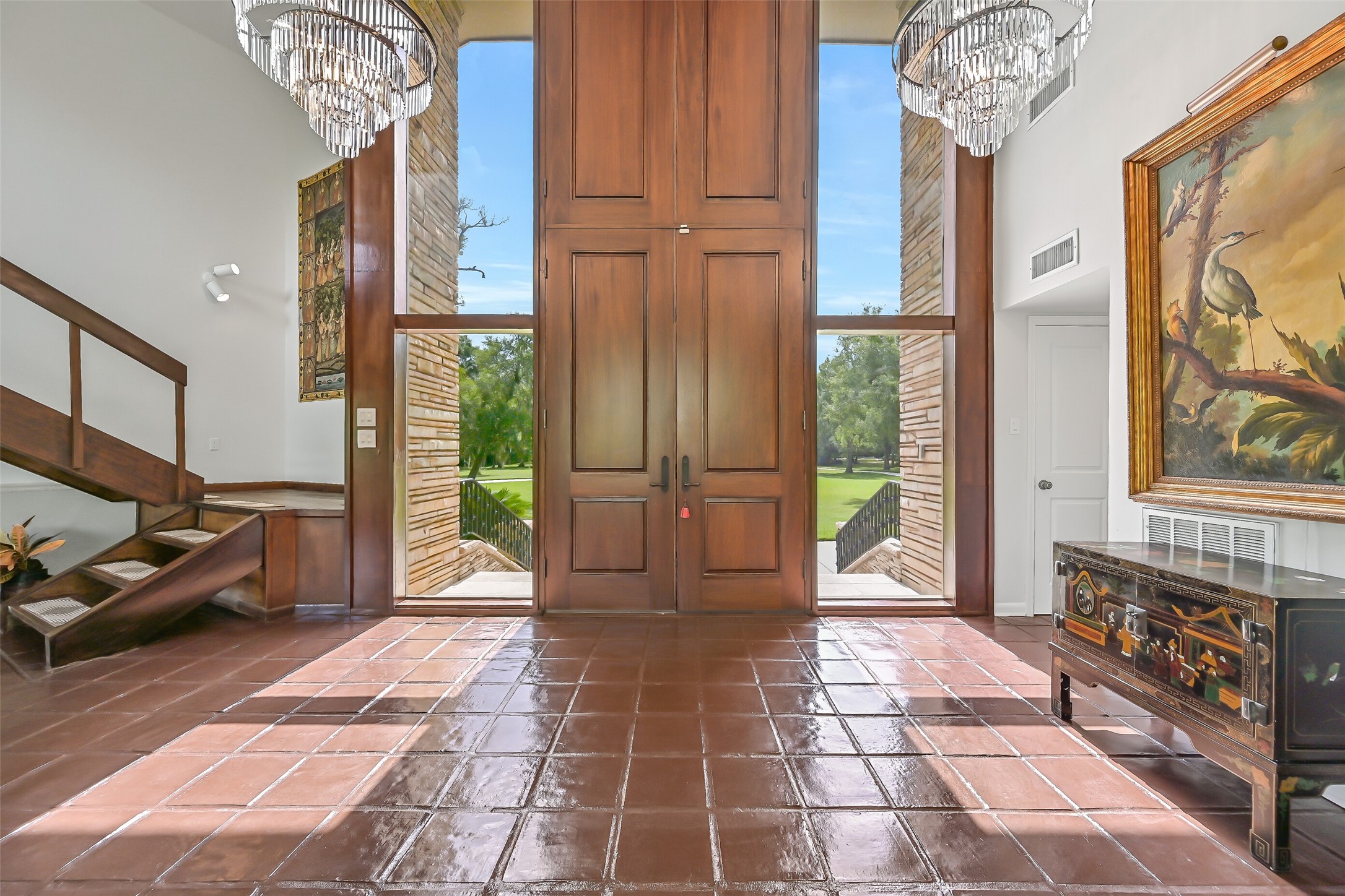 Step inside to a dramatic 17' entry with soaring ceilings, two grand chandeliers & a beautiful open-riser staircase leading to the private upstairs primary suite. The home's distinctive contemporary architecture is immediately apparent, with an inviting view into the sunken living room.