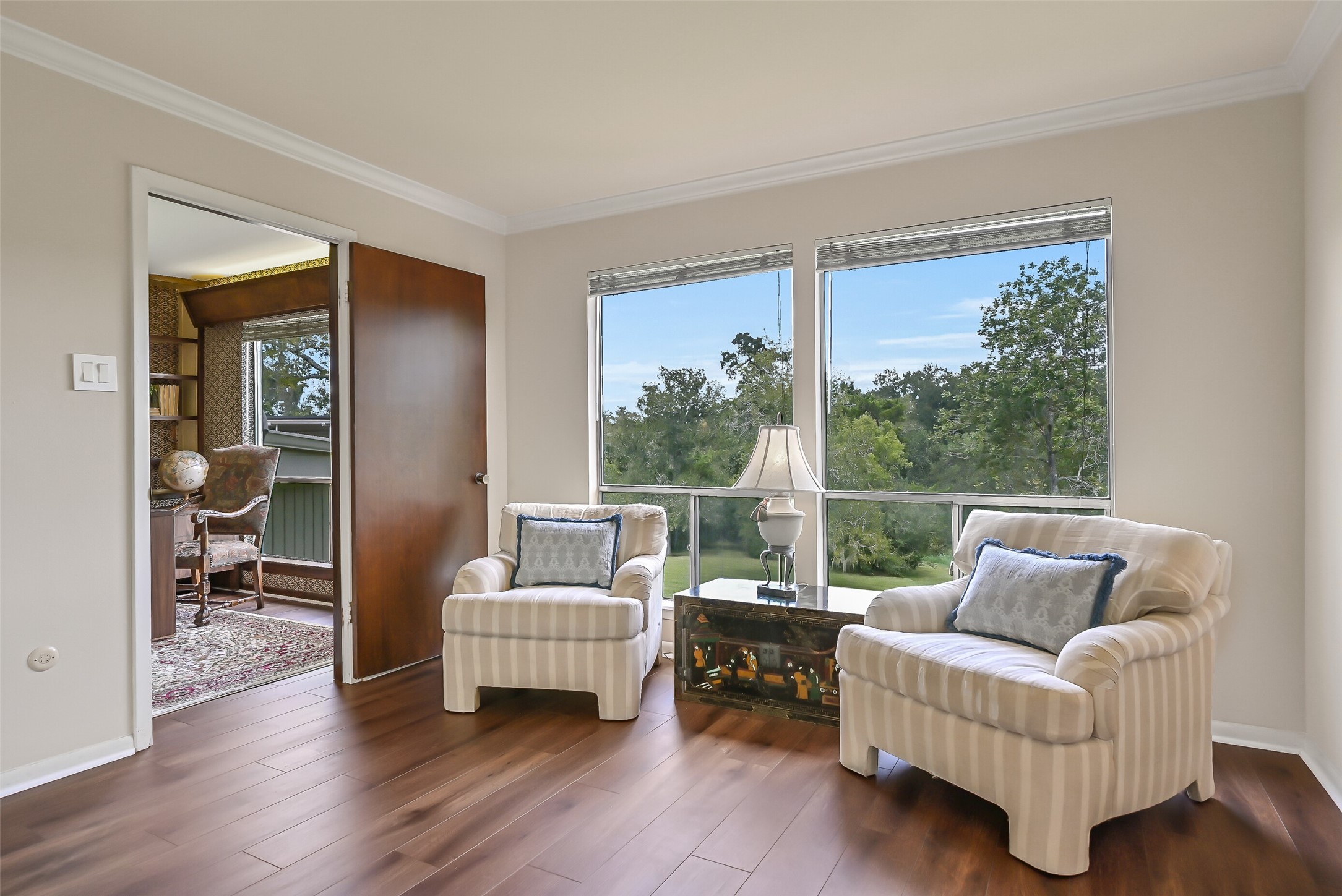 A comfortable sitting area within the upstairs primary suite enjoys beautiful treetop views through two large windows overlooking the acreage. Wood-look flooring, crown molding & neutral finishes create a welcoming space for reading or relaxing, with the adjoining library/office just beyond the doorway.