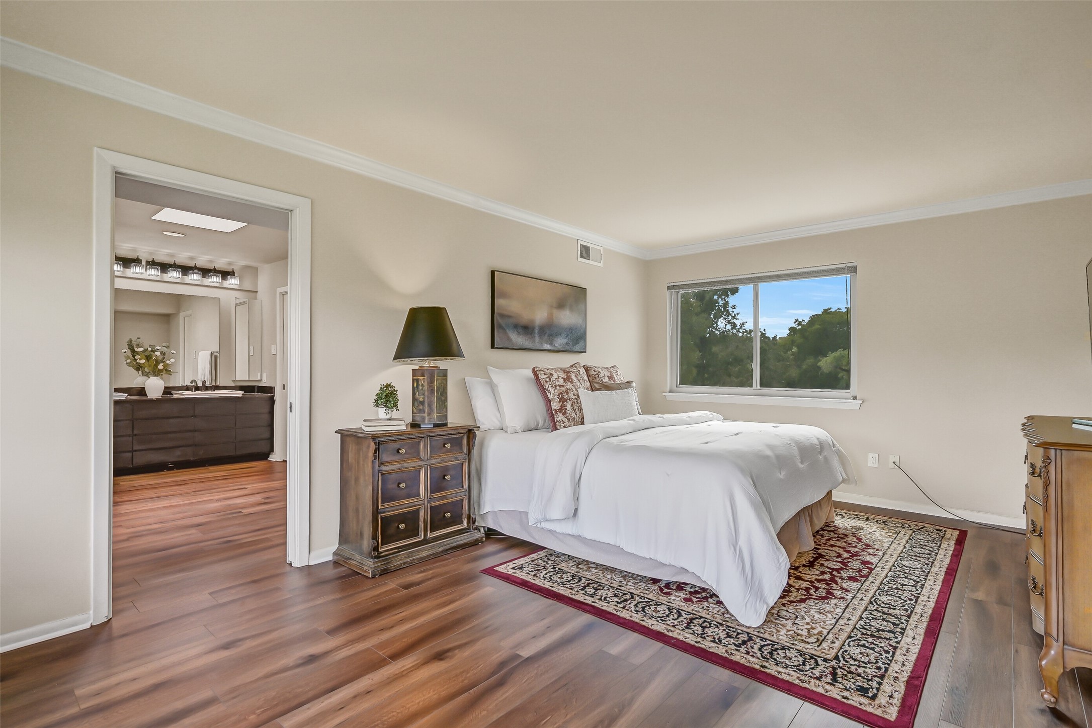 Privately situated on the upper level, the primary suite features wood-look flooring, crown molding & large windows offering views of the surrounding trees. A dedicated sitting area provides additional room to unwind, while the adjoining primary bathroom offers dual sinks & separate bathing spaces.