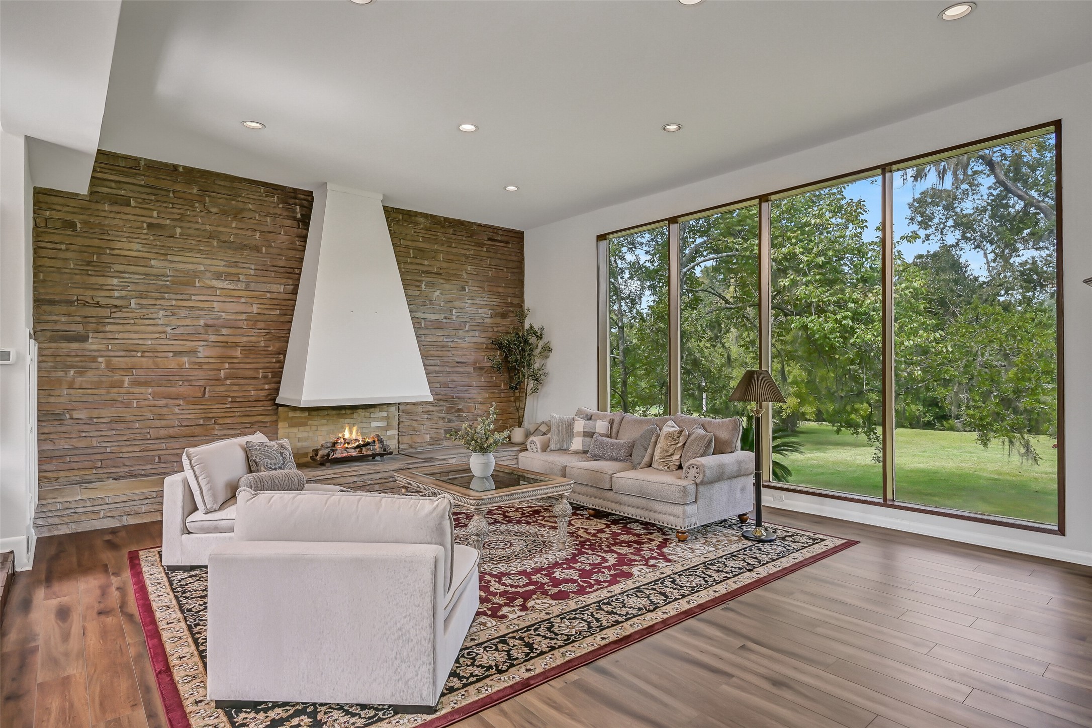 From this perspective, the sunken living room's remarkable size and architectural character are especially apparent. Wood-look flooring, recessed lighting & a 12' ceiling complement the dramatic fireplace, while expansive windows and French doors connect the interior with the outdoor setting.