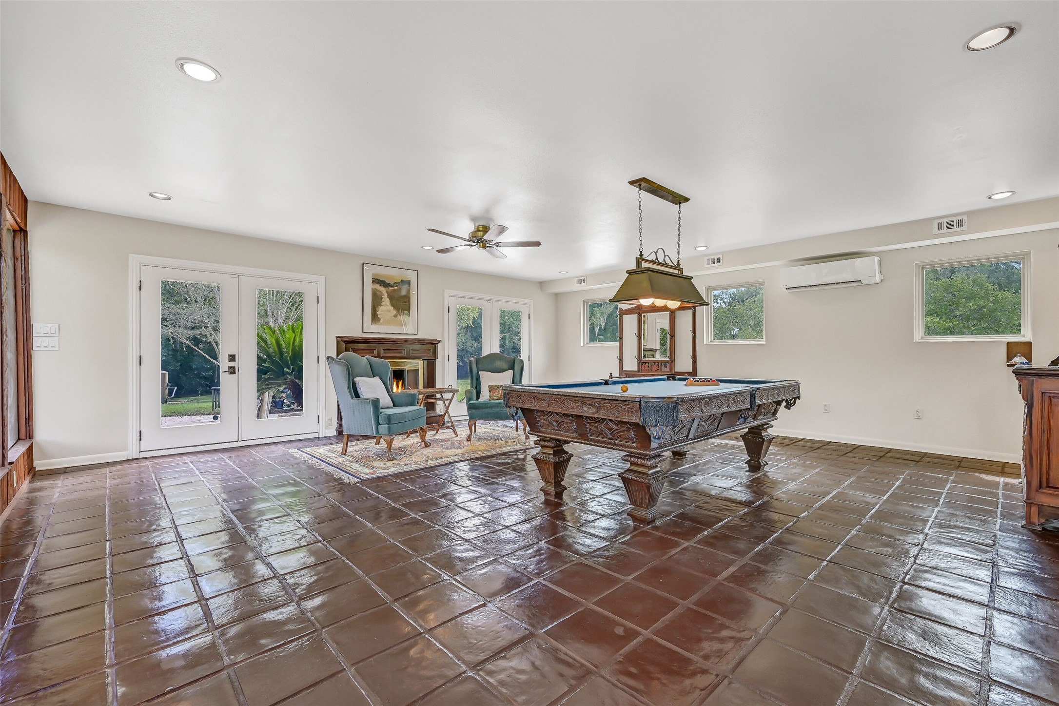 The gameroom's generous dimensions are especially apparent from this angle, with plenty of open floor space surrounding the pool table. Two sets of French doors are visible, providing direct outdoor access, while a gas-log fireplace, supplemental mini-split A/C & recessed lighting add comfort.
