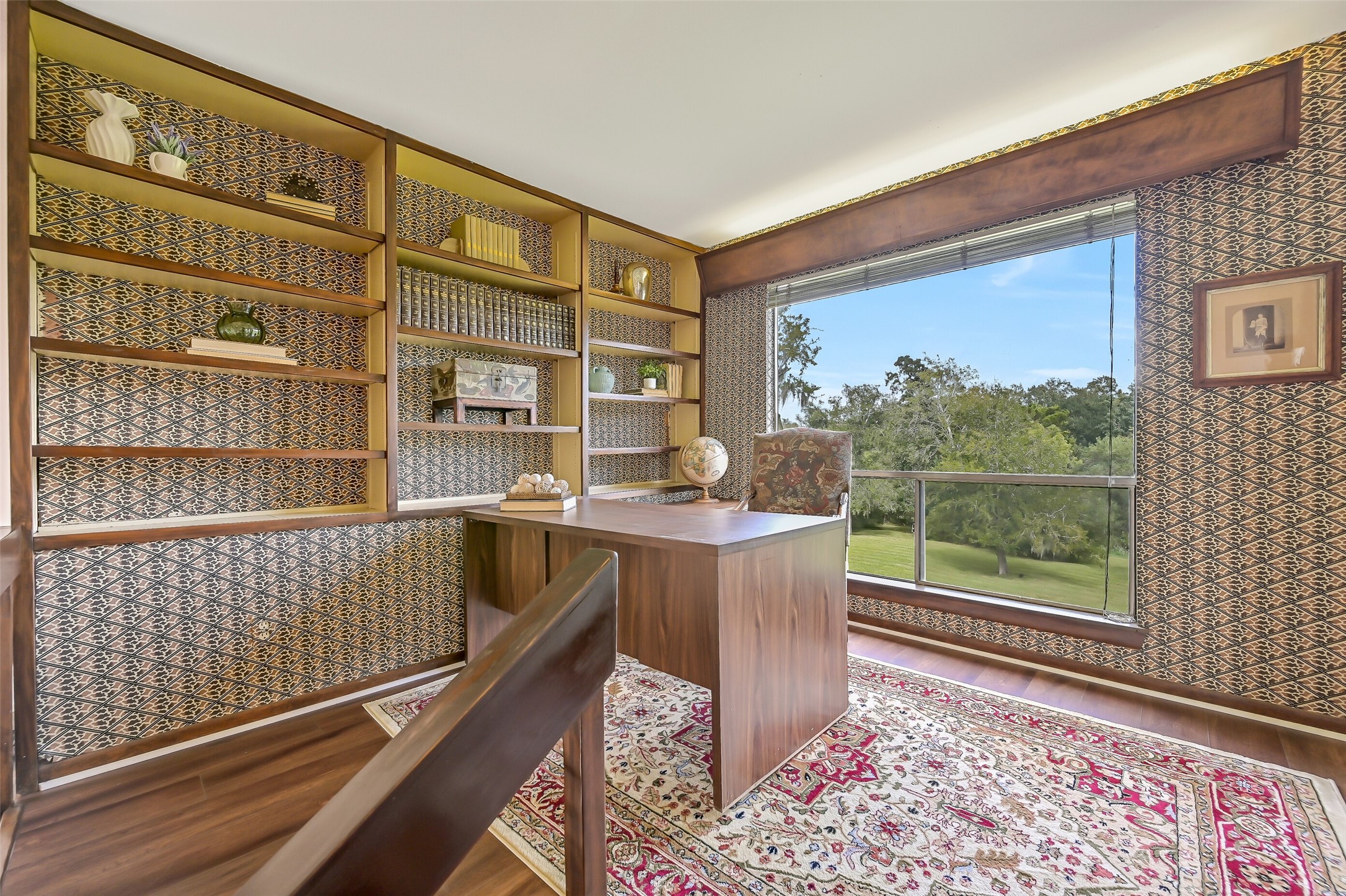 Perched above the main living area, this 10' x 11' library/office features a wall of custom built-in bookshelves, decorative patterned wallpaper & wood-look flooring. A large picture window overlooks the property's mature trees & sprawling grounds, creating a quiet, light-filled workspace.
