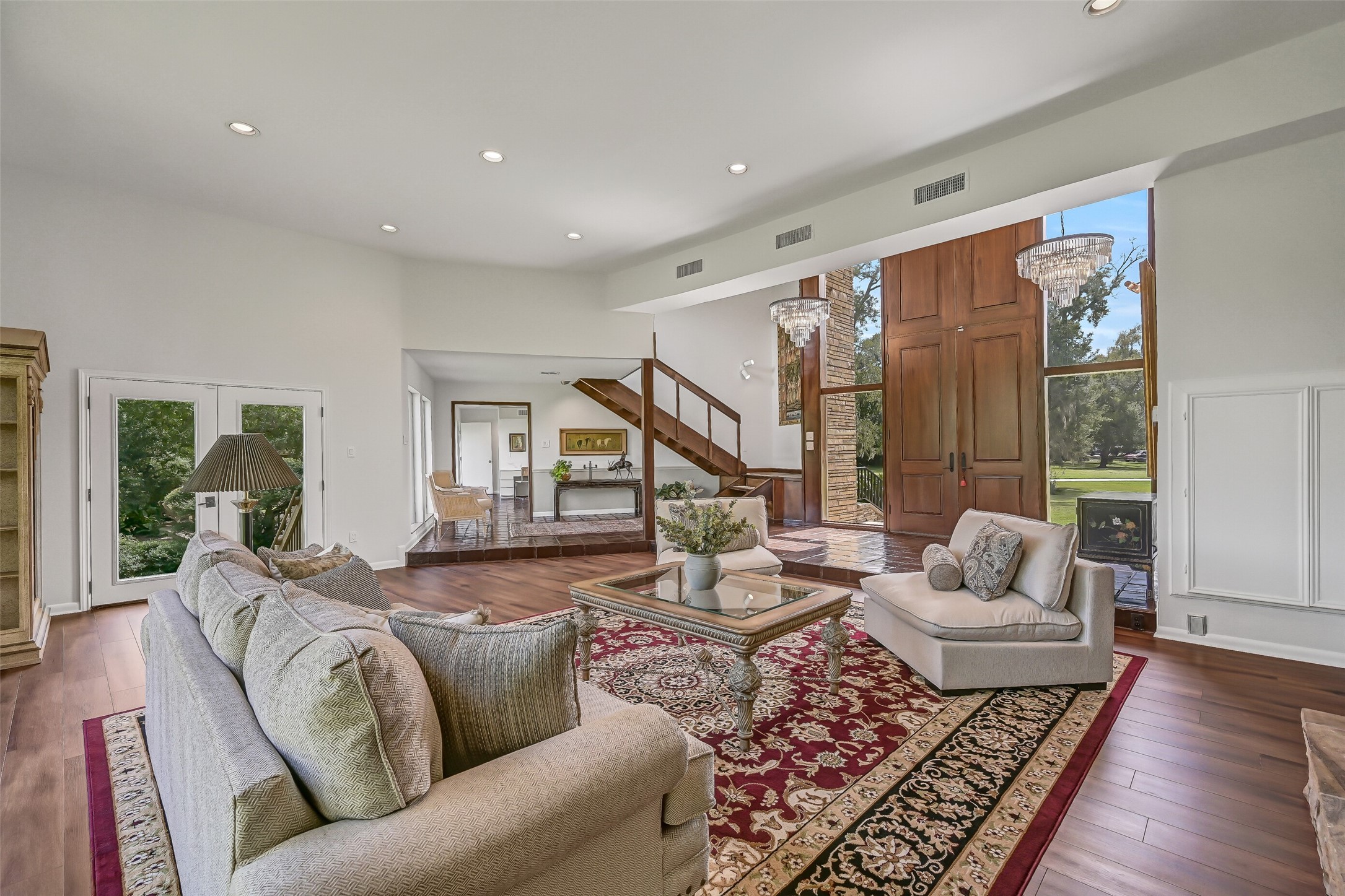 The living room opens toward the home's grand entry, where the open-riser staircase and soaring ceiling create an interesting architectural contrast. With approximately 783 square feet, this generous gathering space offers abundant room for comfortable seating and entertaining.