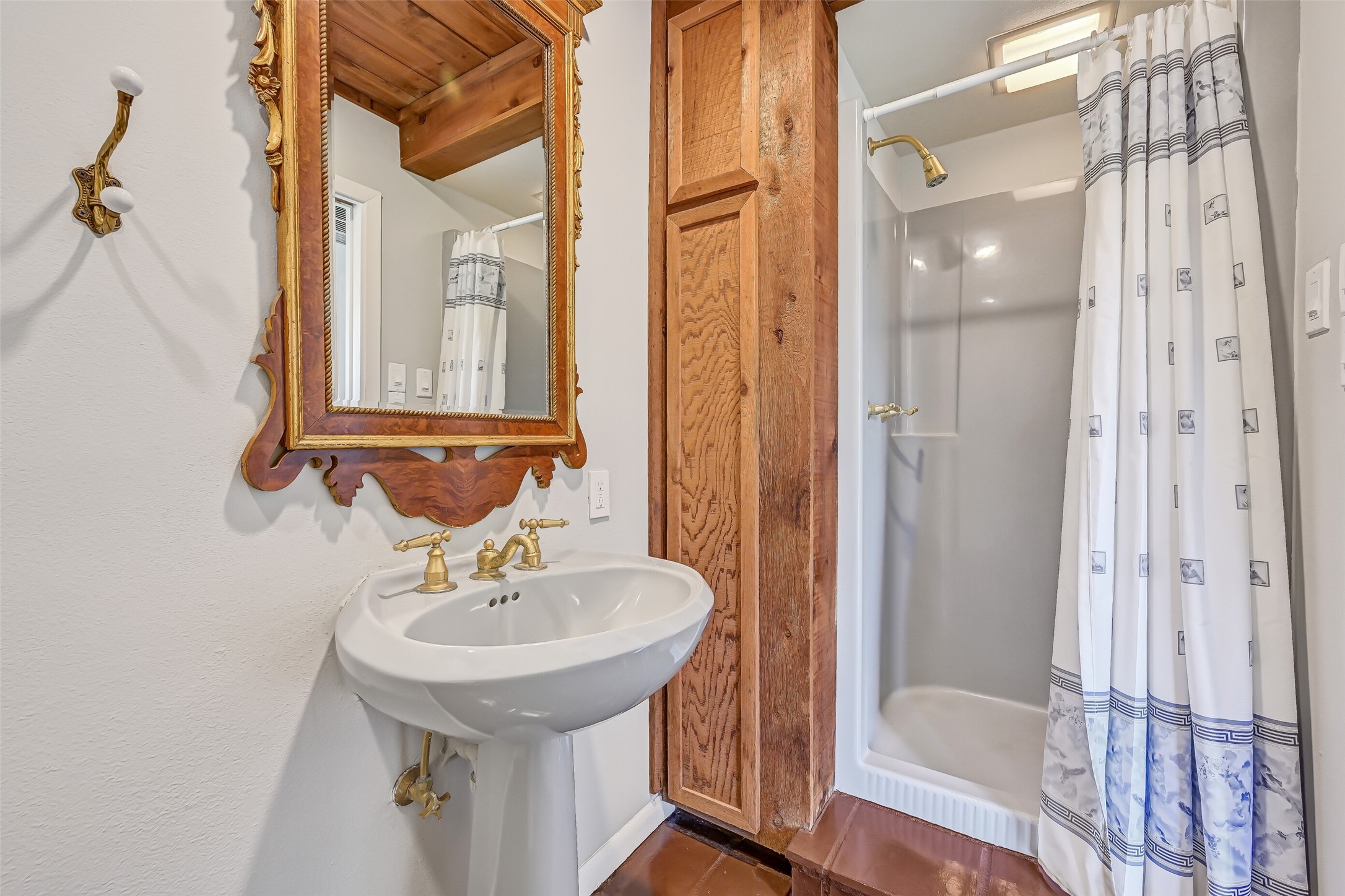 Conveniently located near the prefvious bedroom, kitchen & gameroom, this full bathroom features a pedestal sink with gold-tone fixtures, decorative mirror, stand-up shower & distinctive wood cabinetry. Its location makes it easily accessible from the adjoining living spaces.