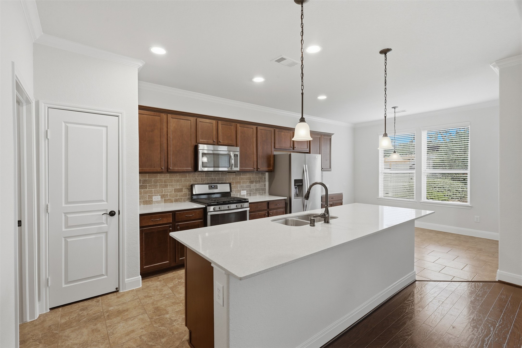 Open island kitchen with quartz countertops, stainless steel appliances, abundant cabinetry, recessed lighting, and breakfast area, all flowing seamlessly into the dining and living spaces.