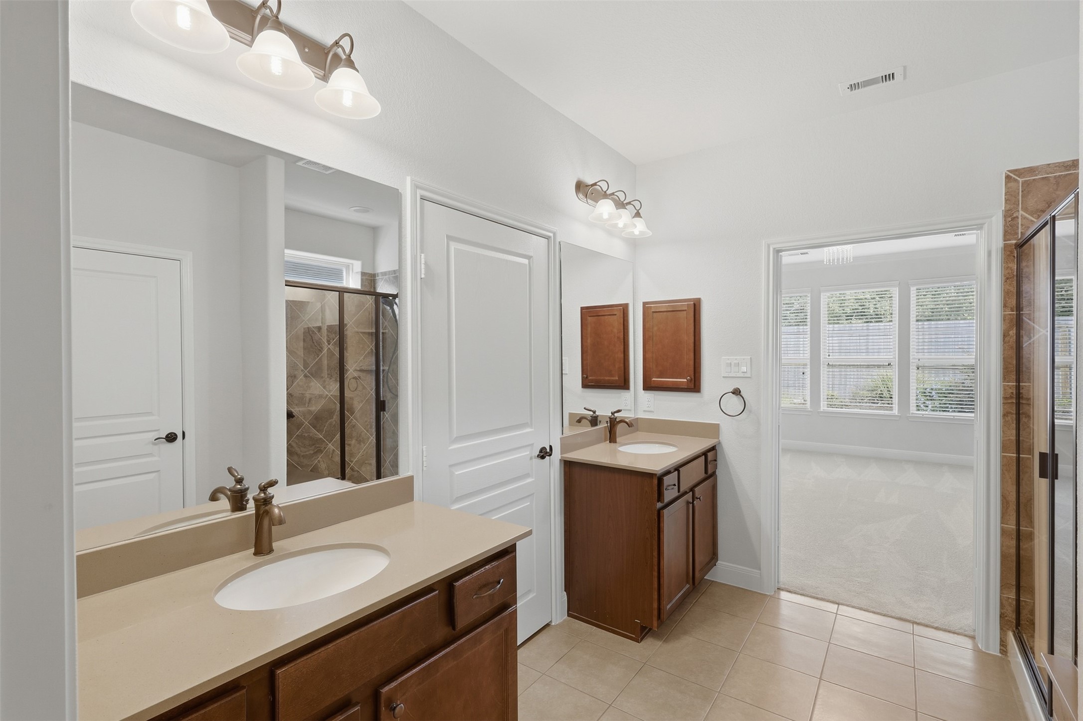 Primary bathroom featuring separate vanities, generous counter space, and an oversized walk-in shower with tile, glass enclosure, and built-in bench. The large walk-in closet provides excellent storage and convenient access directly from the primary bath.