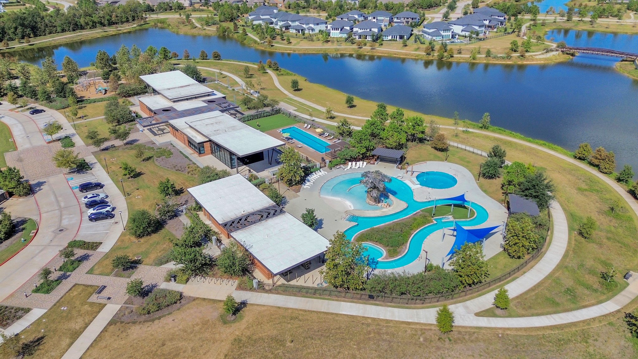 The aerial view captures the community's resort-style pool and scenic walking trail winding around the lake, providing a picturesque setting for relaxation and outdoor activities.