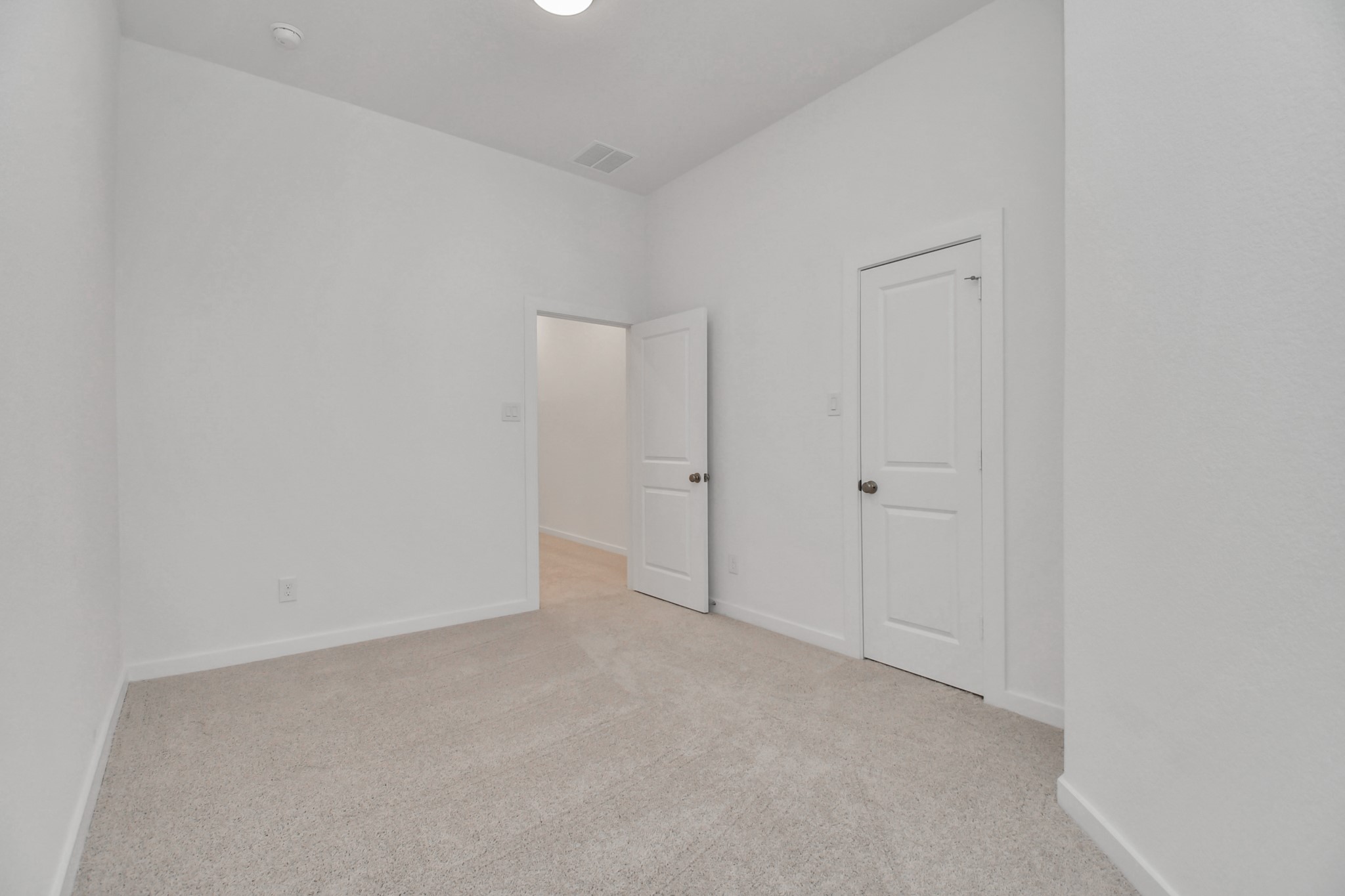 The secondary bedroom is bright and airy with a white color scheme and plush carpet, offering a comfortable and inviting space.