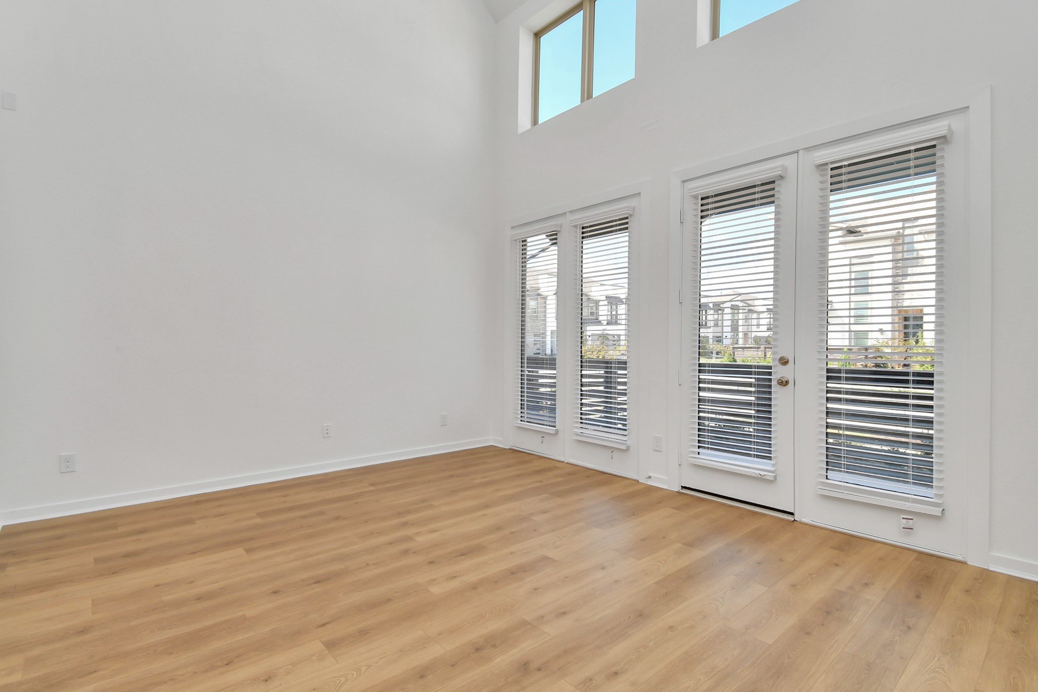 The living room features soaring high ceilings and expansive windows that fill the space with light, along with direct access to the front patio for easy indoor-outdoor living.