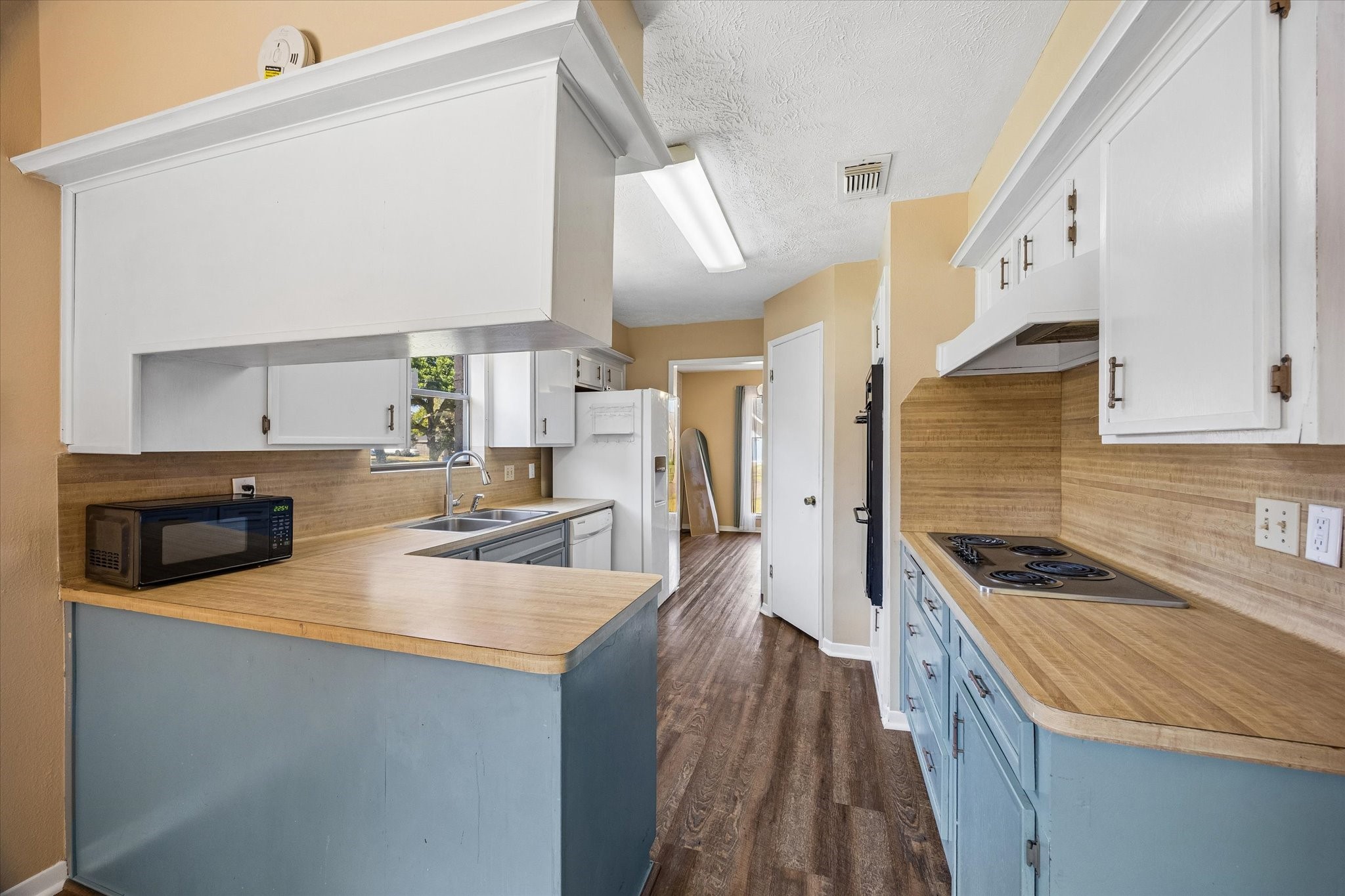 Charming kitchen with a cozy layout featuring white cabinetry and a convenient breakfast bar. The space is accented by warm-toned walls and natural light from a window above the sink.