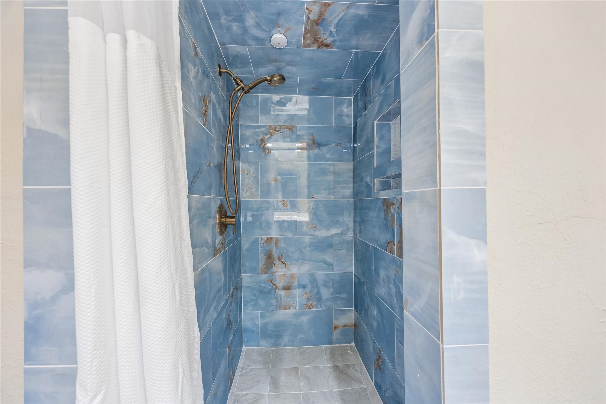 Luxurious shower with stunning blue marble-like tiles and a sleek bronze showerhead, offering a serene spa-like experience.