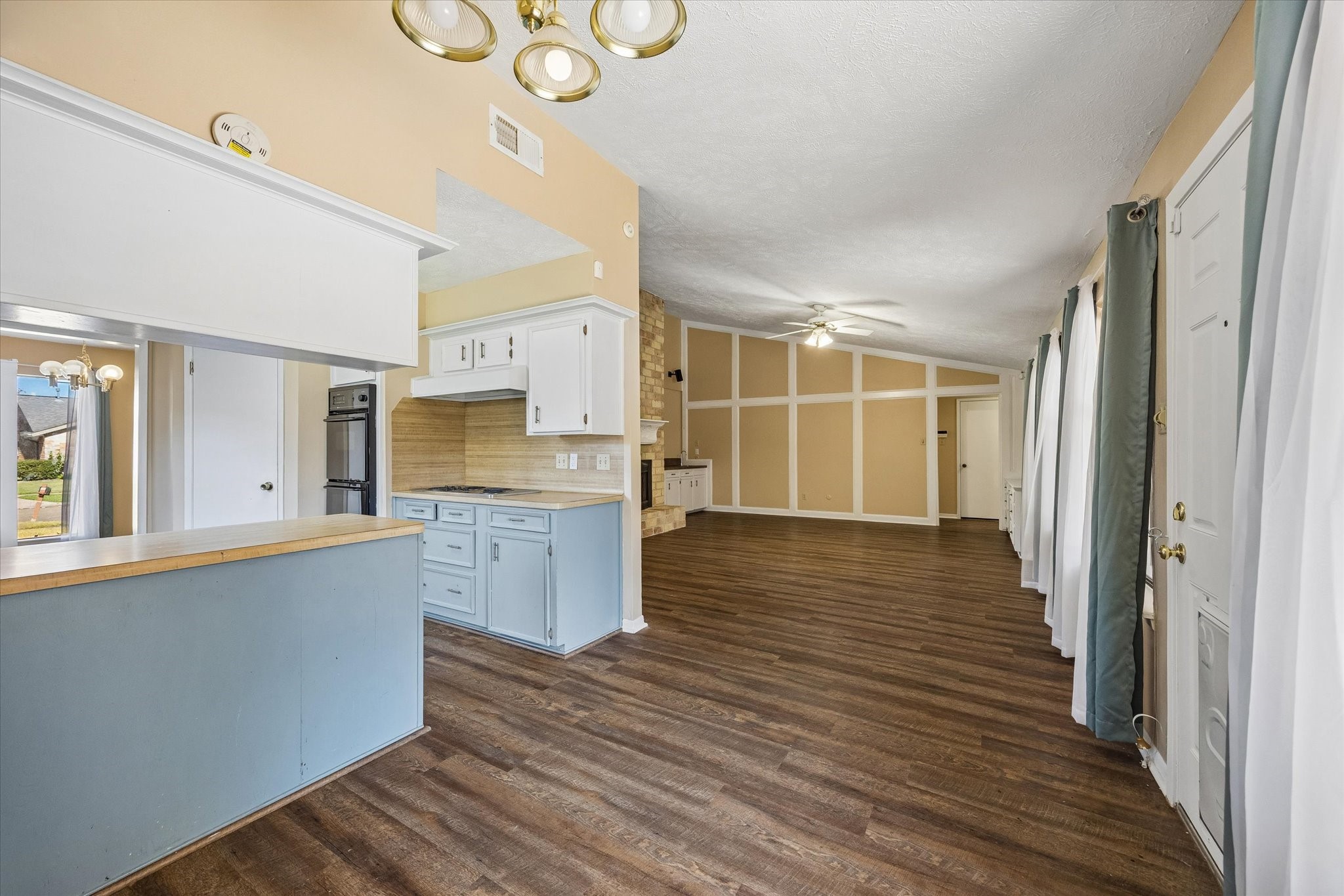 Spacious open-concept living area with elegant wood flooring, a cozy kitchen with light cabinetry, and abundant natural light from large windows.