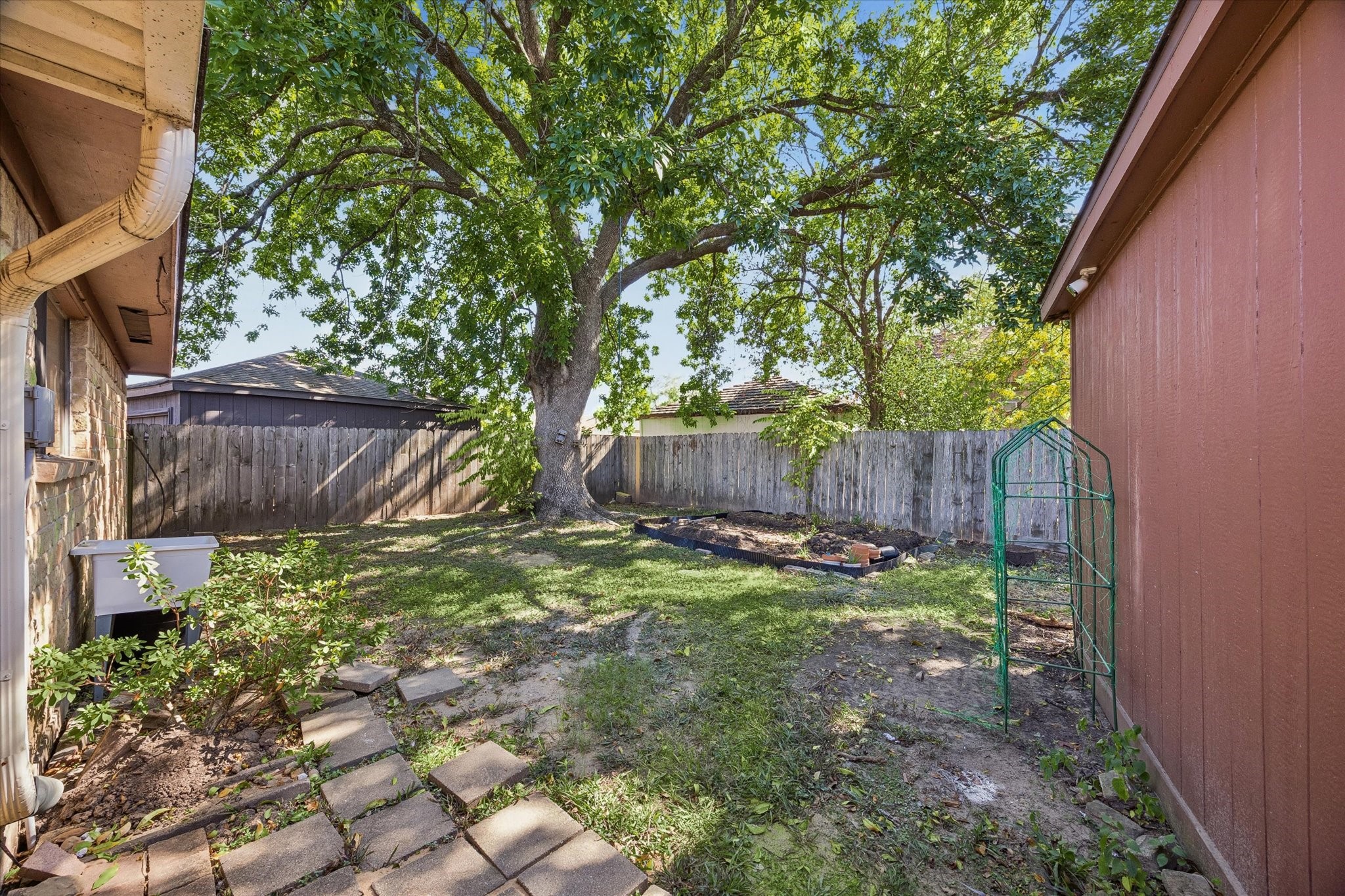 Charming backyard with a large, shady tree and ample space for gardening or relaxation, enclosed by a wooden fence for privacy.