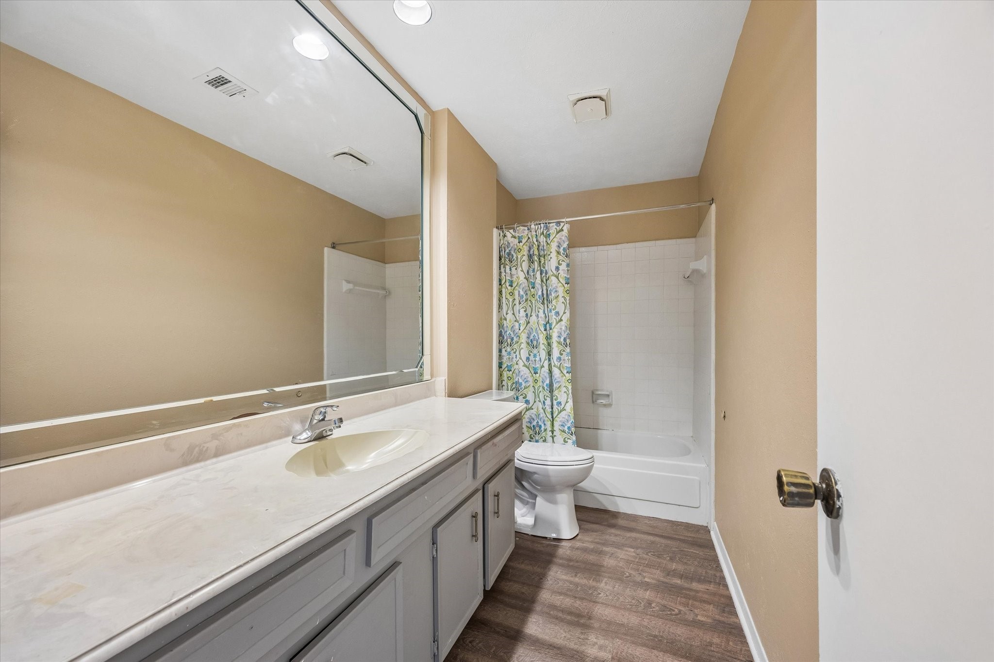 Spacious bathroom featuring a large mirror, elegant vanity, and a classic shower-tub combination.