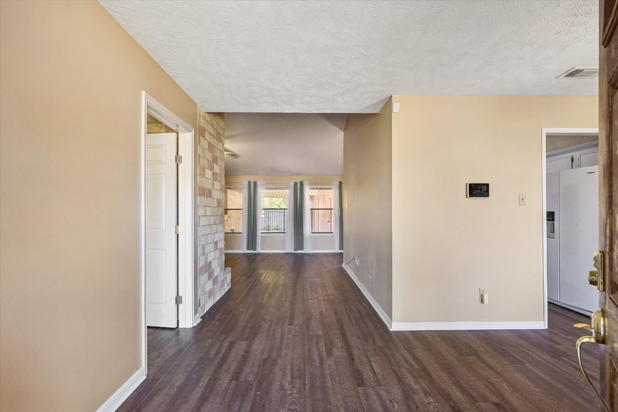 Inviting entryway with warm-toned walls and rich flooring, leading to a bright living area enhanced by large windows and a stone accent wall.