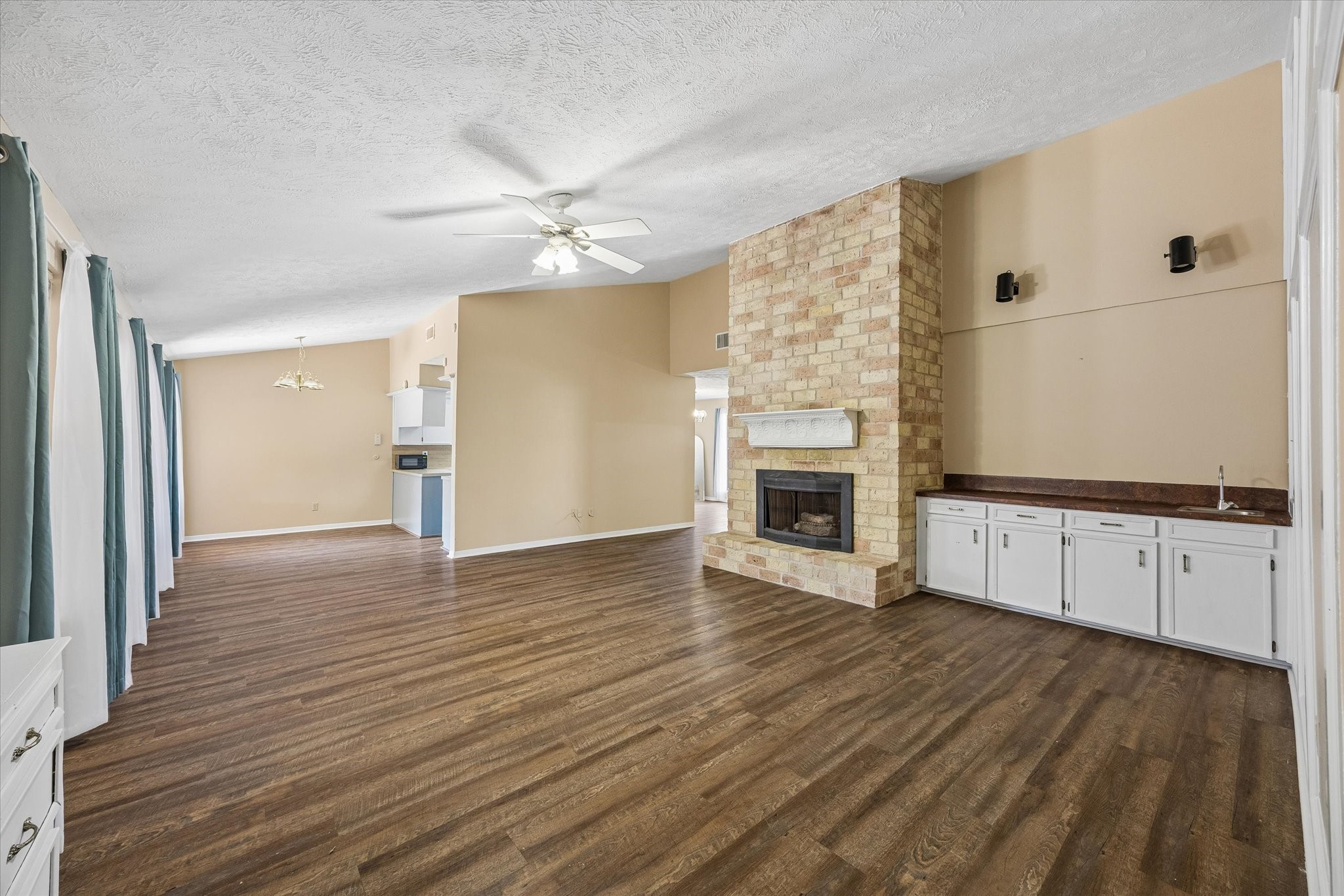 Spacious open living area featuring a charming brick fireplace, and abundant natural light from expansive windows. The room offers a seamless flow to the dining area and kitchen, ideal for entertaining.