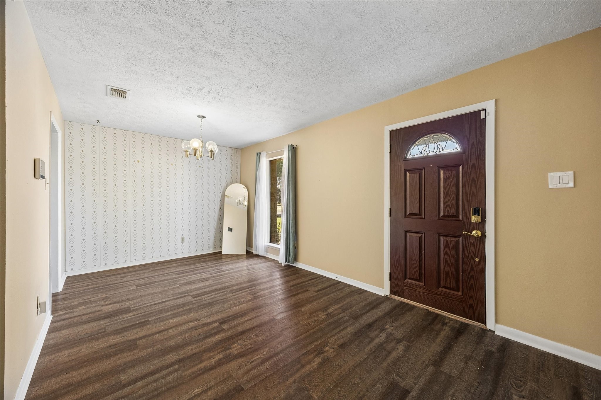 Inviting entryway with rich flooring, a stylish dark wood front door, and a cozy dining area adorned with a classic wallpaper accent.