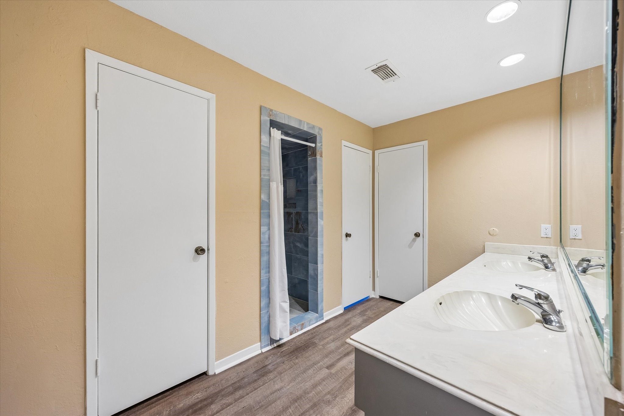 Spacious bathroom featuring a dual-sink vanity, warm-toned walls, and a sleek, tiled shower area.