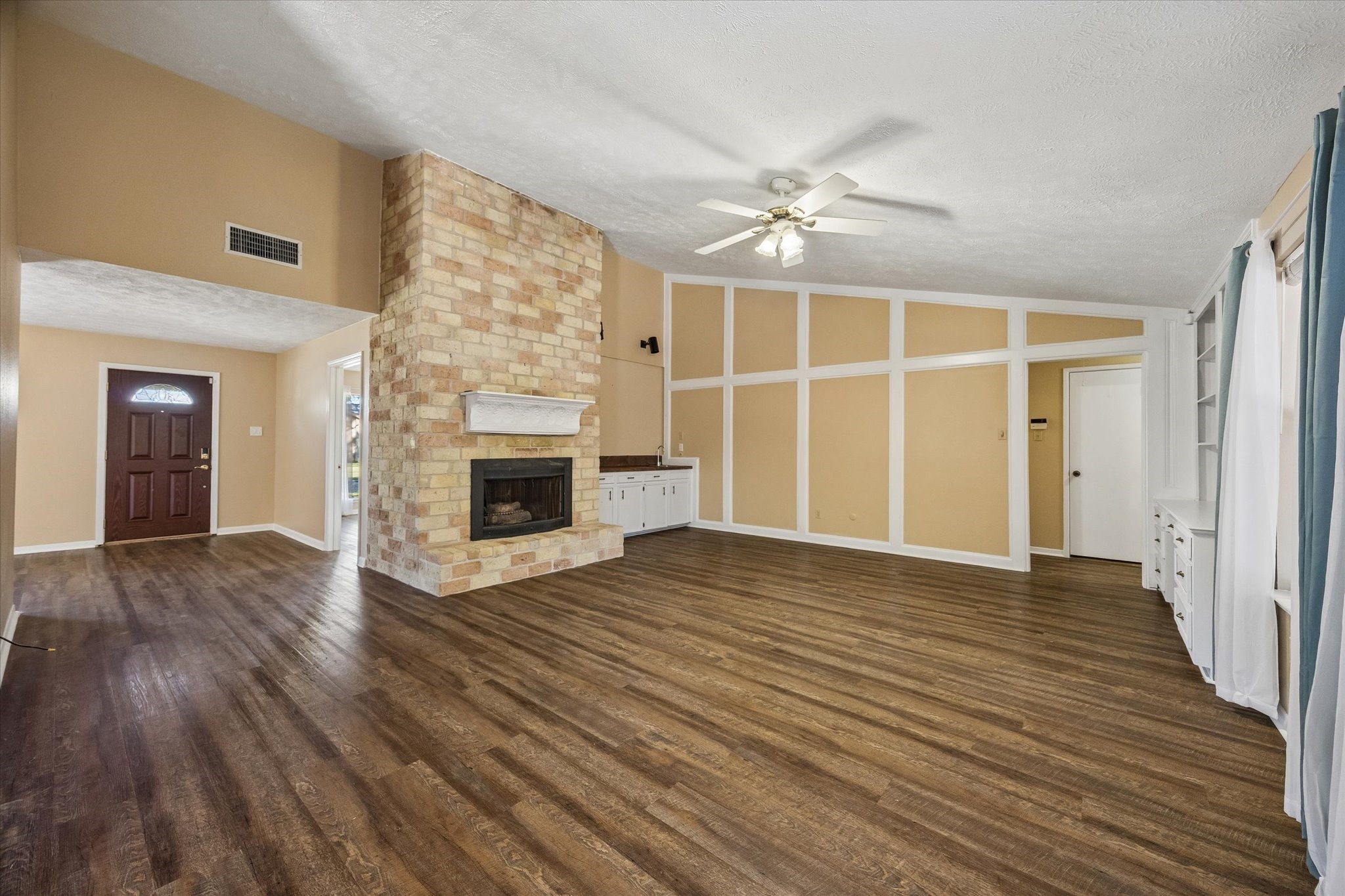 Spacious living room with rich floors and a striking brick fireplace, perfect for cozy evenings. Elegant built-in shelving adds character, while large windows fill the space with natural light.