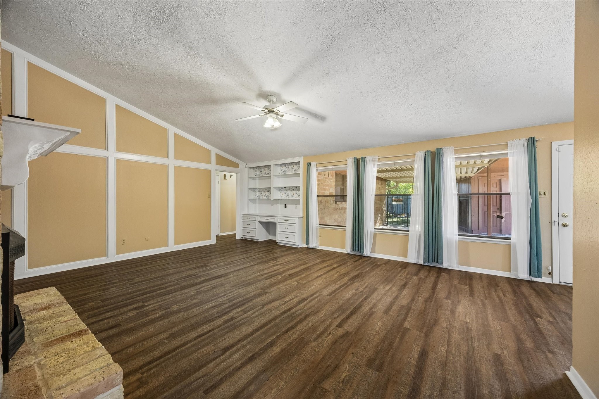 Spacious living room featuring large windows with stylish curtains offering ample natural light, built-in shelving, and a cozy fireplace, perfect for family gatherings.