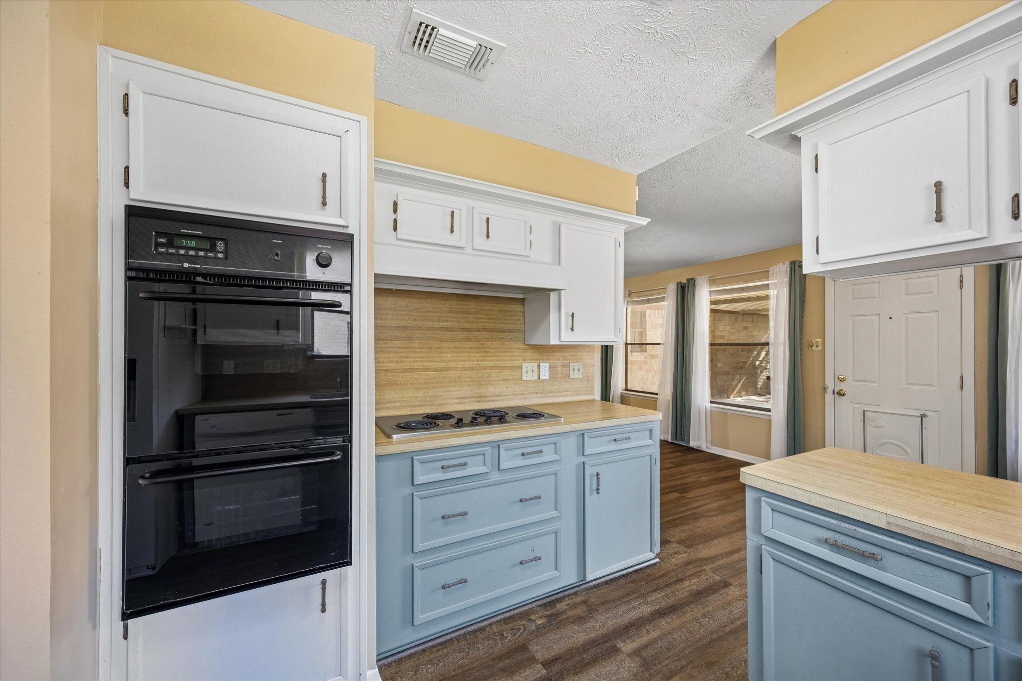 Charming kitchen with retro flair features a double oven, electric cooktop, and a blend of white and blue cabinetry, complemented by warm wood accents and natural light.