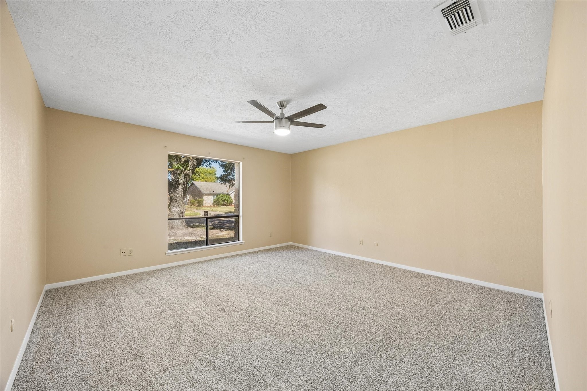 Spacious bedroom with neutral walls, plush carpet, a modern ceiling fan, and a large window offering natural light.
