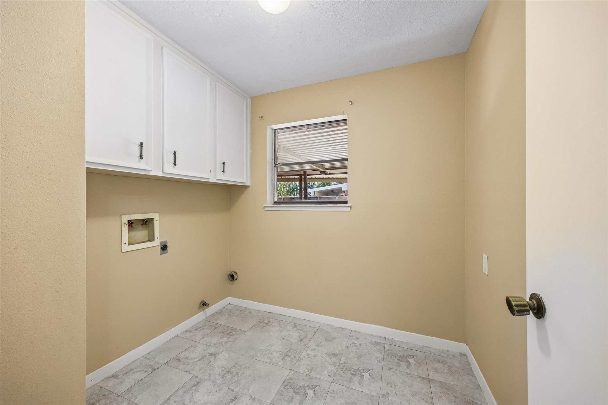 Bright laundry room with ample cabinet storage, a window for natural light, and tiled flooring for easy maintenance.