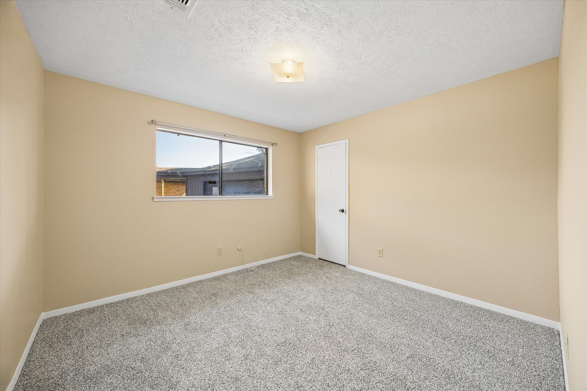 Spacious bedroom with neutral walls, plush carpeting, and a large window for natural light.