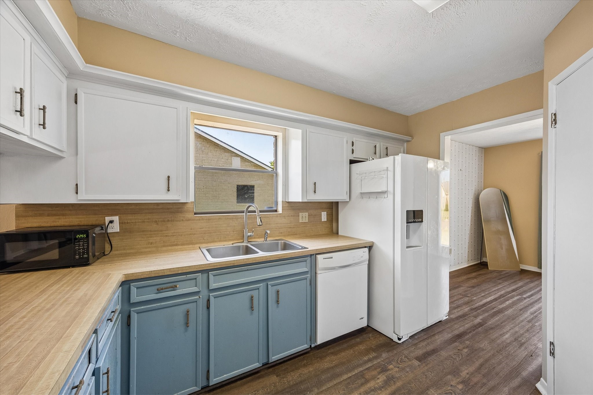 Charming kitchen with two-tone cabinetry, sleek countertops, and a large window providing natural light. Features include a double sink, dishwasher, and spacious fridge, perfect for culinary enthusiasts.