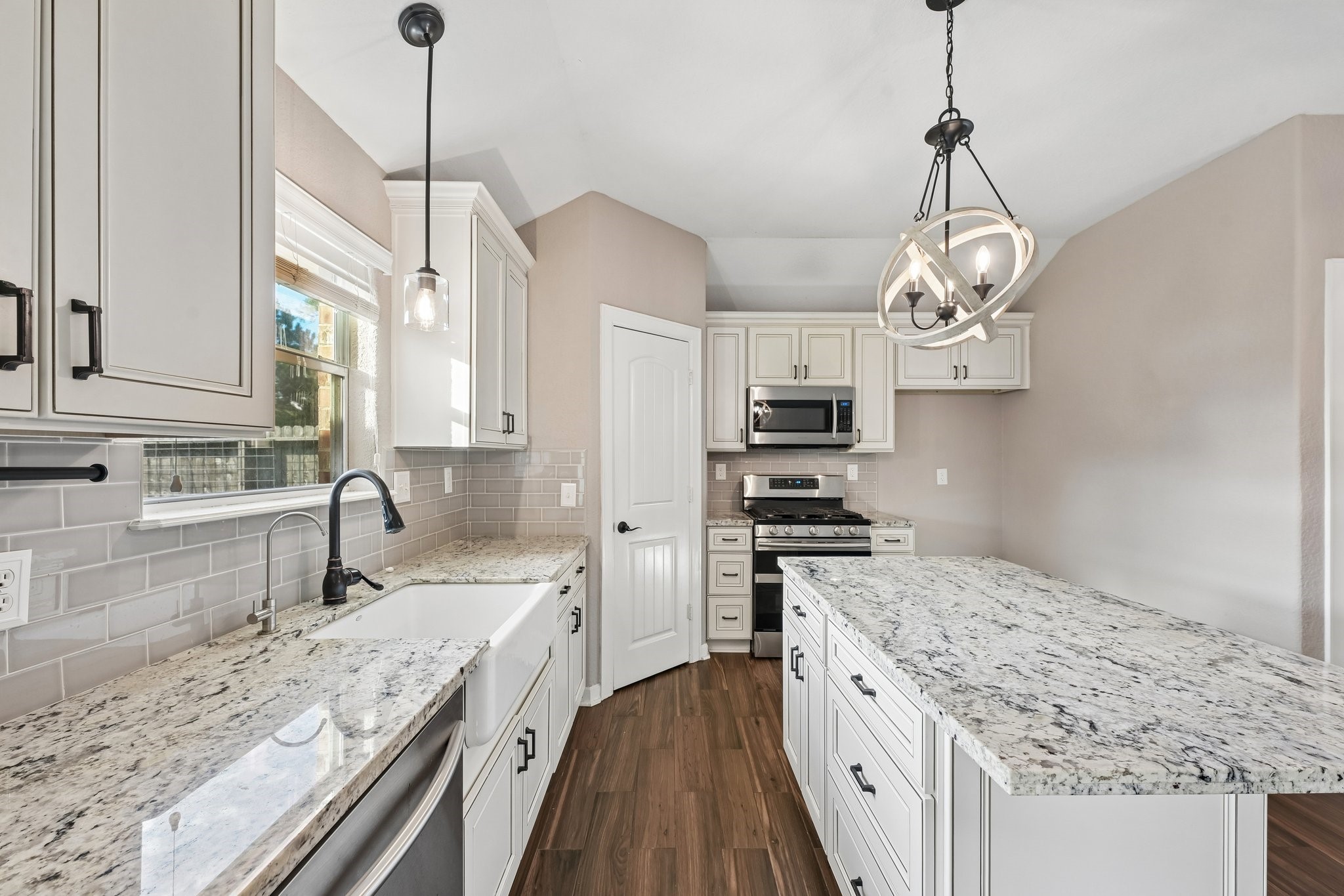 Bright and inviting kitchen featuring elegant granite countertops, modern stainless steel appliances, and stylish pendant lighting, complemented by warm wood flooring.
