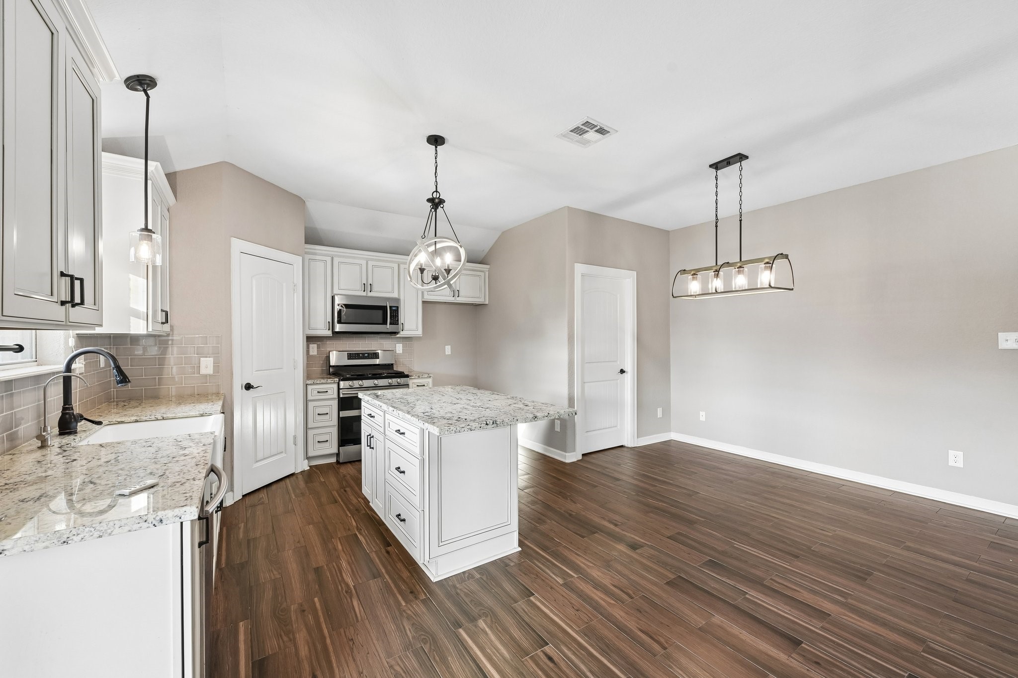 Modern kitchen with elegant granite countertops, stainless steel appliances, and stylish pendant lighting, seamlessly flowing into a spacious living area with rich wood flooring.