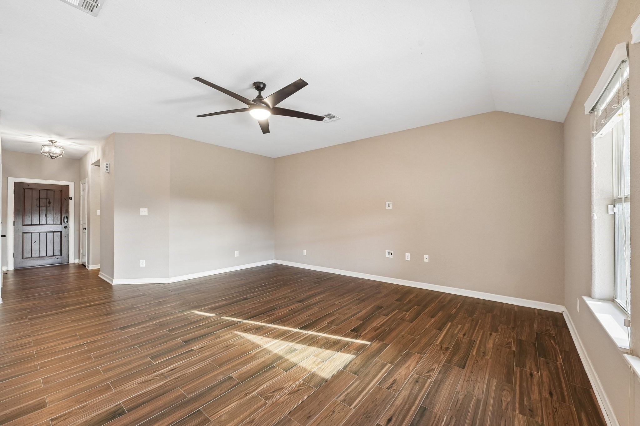Spacious living area with elegant wood-look flooring, neutral walls, and abundant natural light, complemented by a modern ceiling fan.