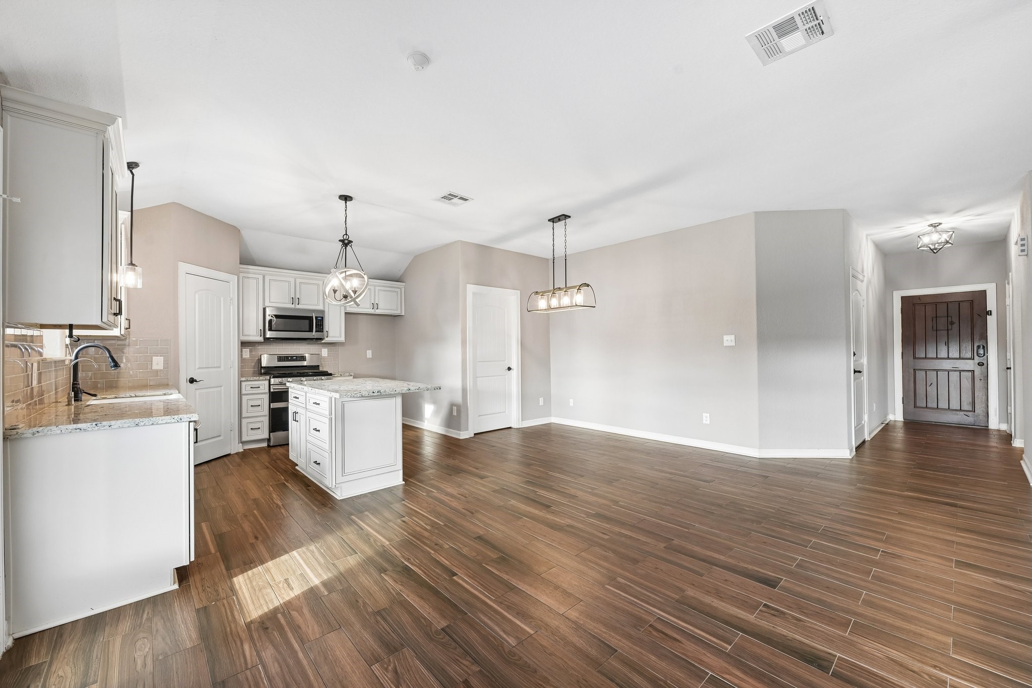 Spacious open-concept kitchen and living area featuring elegant wood flooring, modern stainless steel appliances, and stylish pendant lighting, perfect for entertaining.
