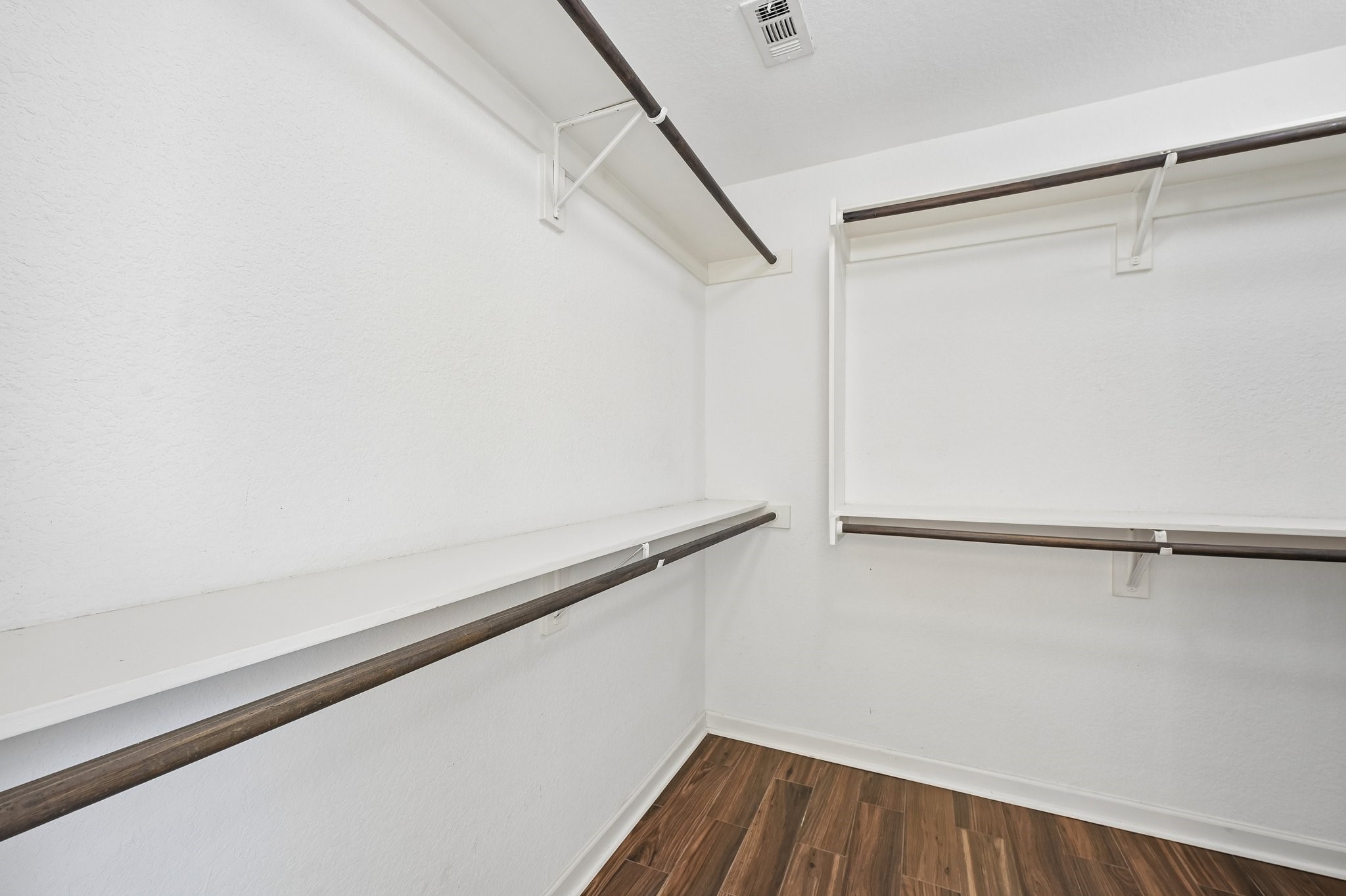 Spacious walk-in closet featuring sleek wooden flooring and ample shelving for organized storage.