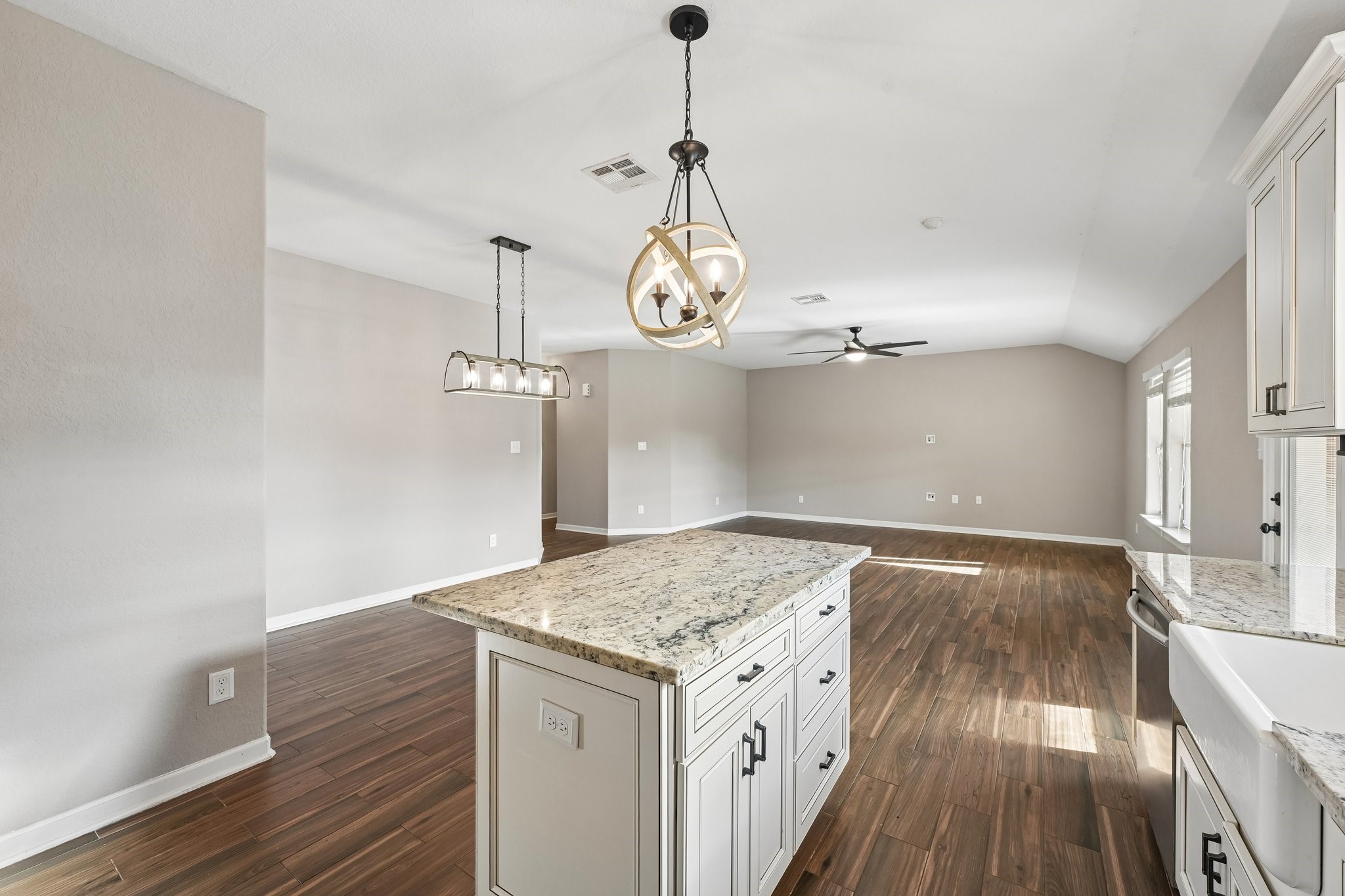 Bright and spacious open-plan living area featuring elegant wood floors, a modern kitchen island with granite countertops, and stylish pendant lighting.