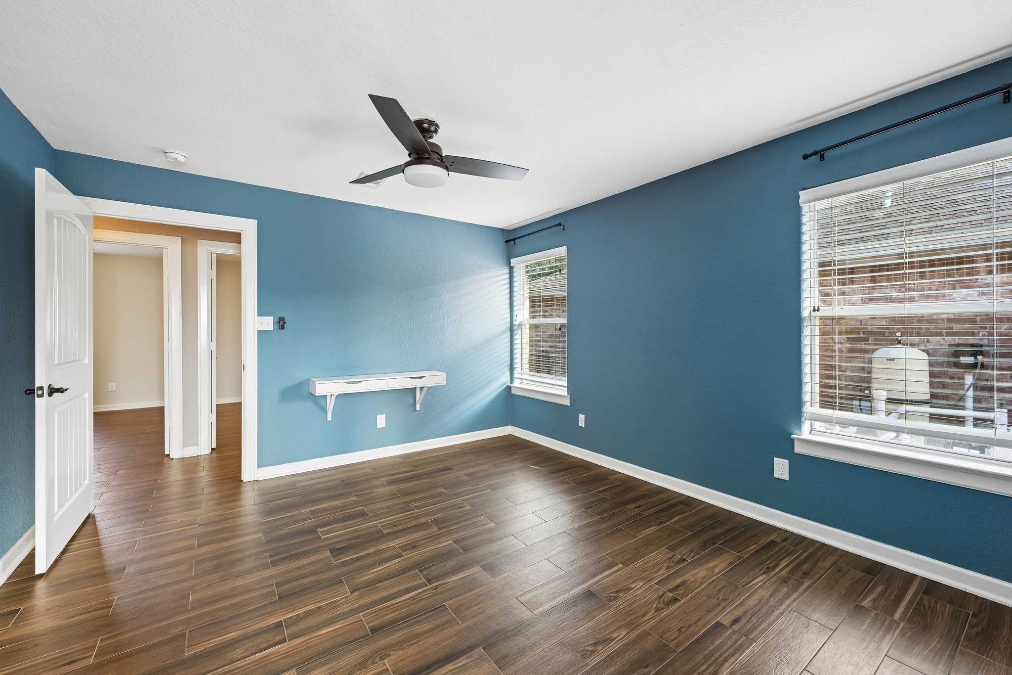 Spacious bedroom with rich wood flooring, calming blue walls, and ample natural light from large windows.