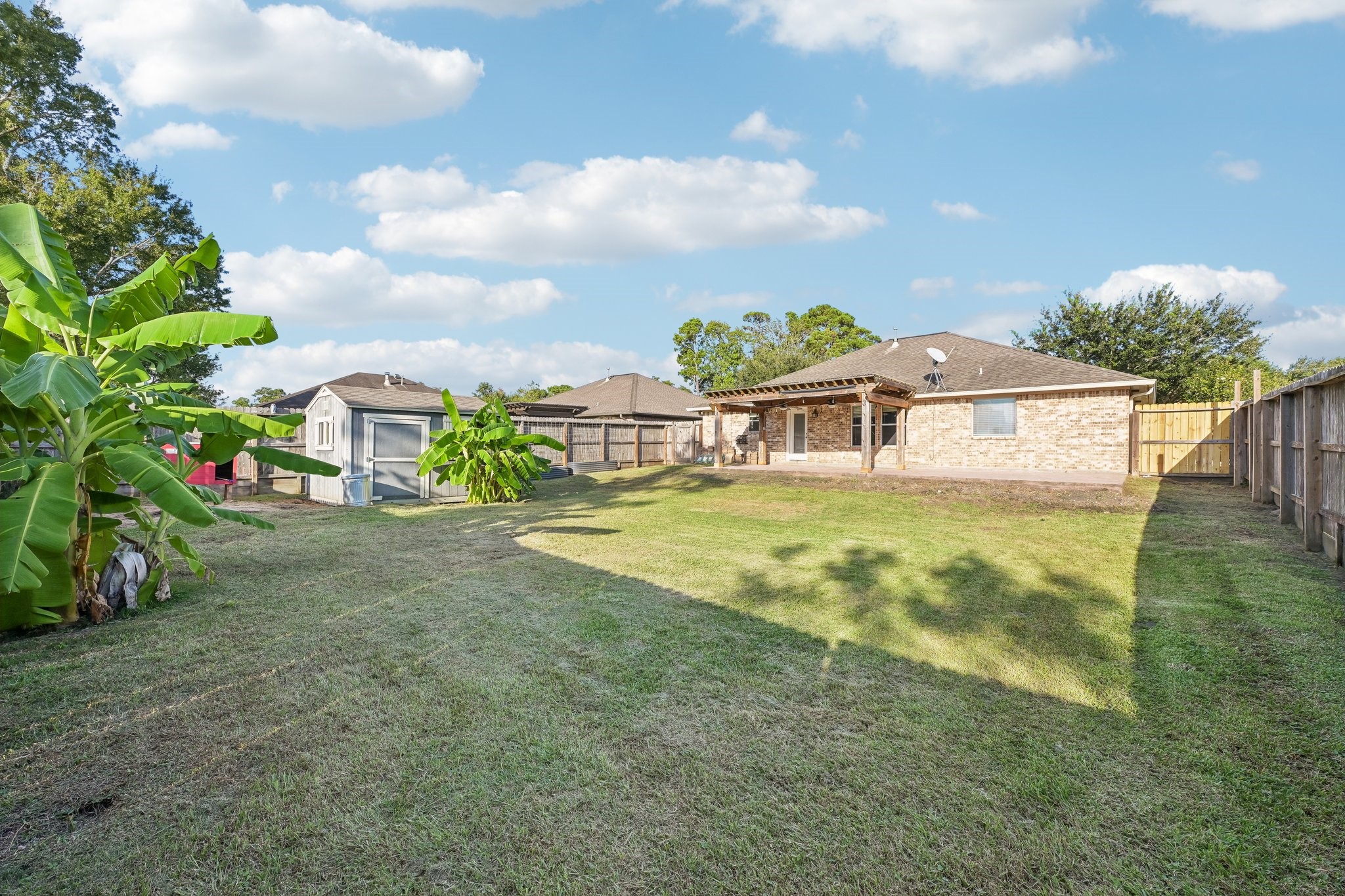 Expansive backyard with lush greenery and a spacious covered patio, perfect for outdoor activities and relaxation.